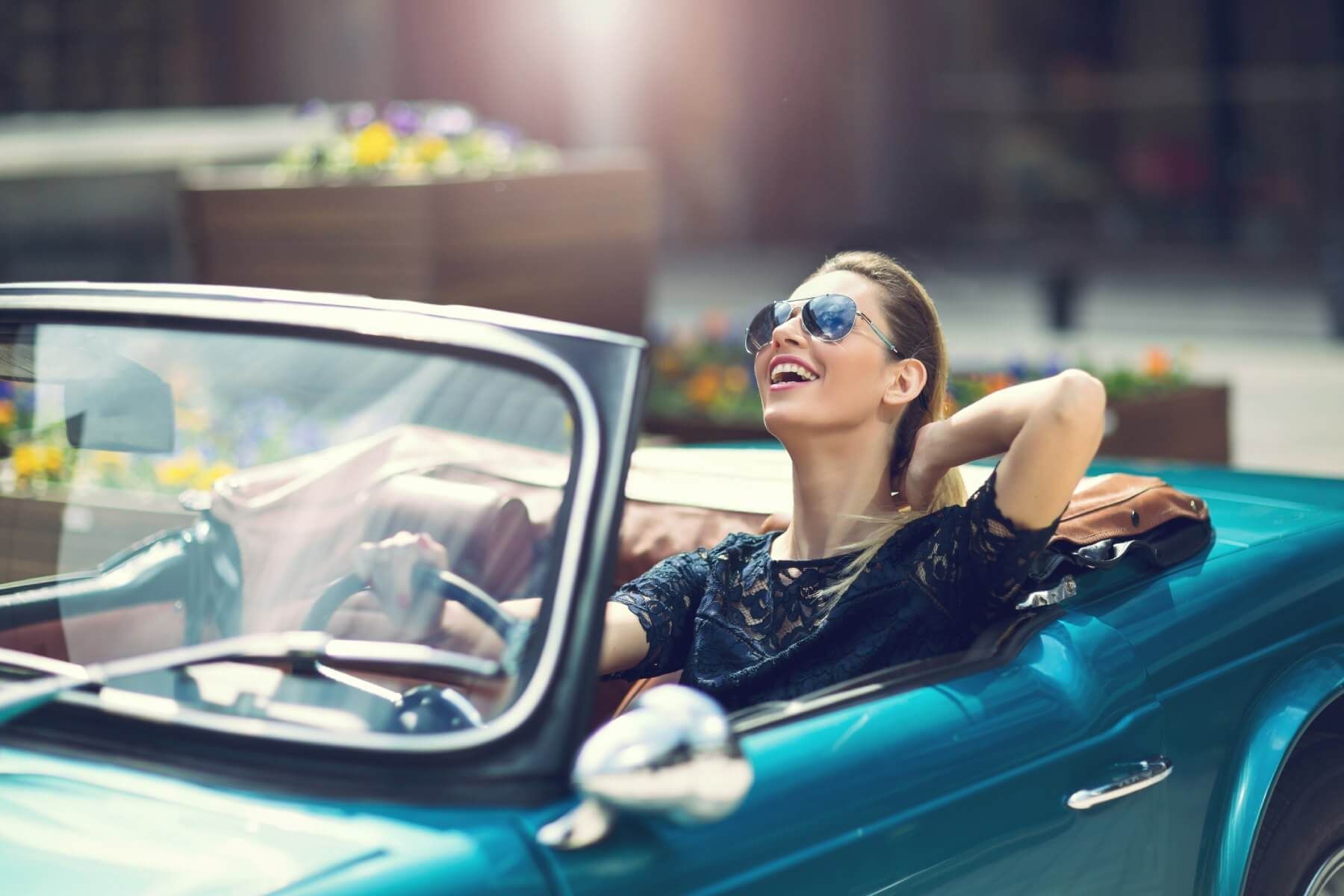 a woman wearing sunglasses is sitting in a blue convertible car .