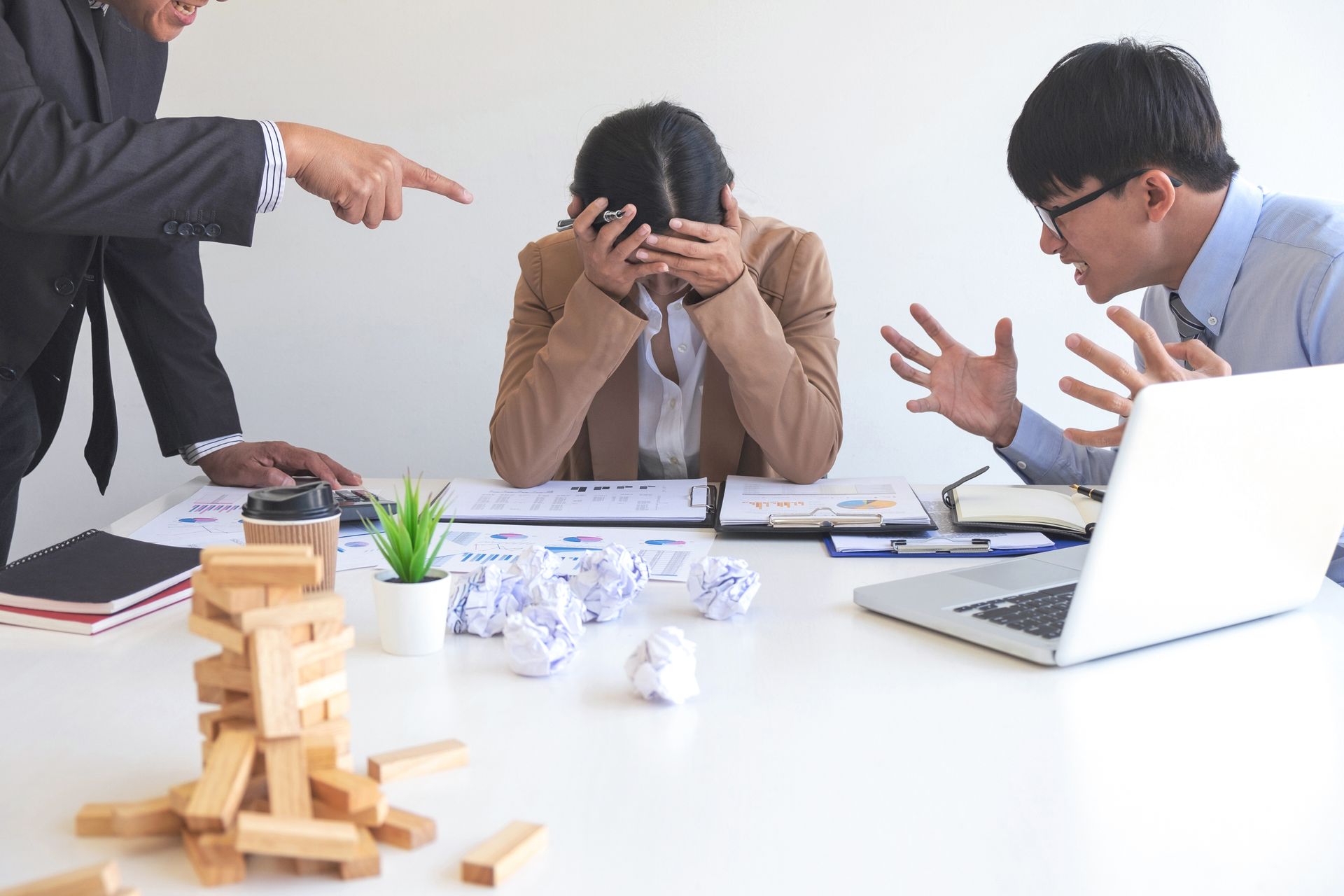 People in office arguing, woman with hands on face, looking stressed.
