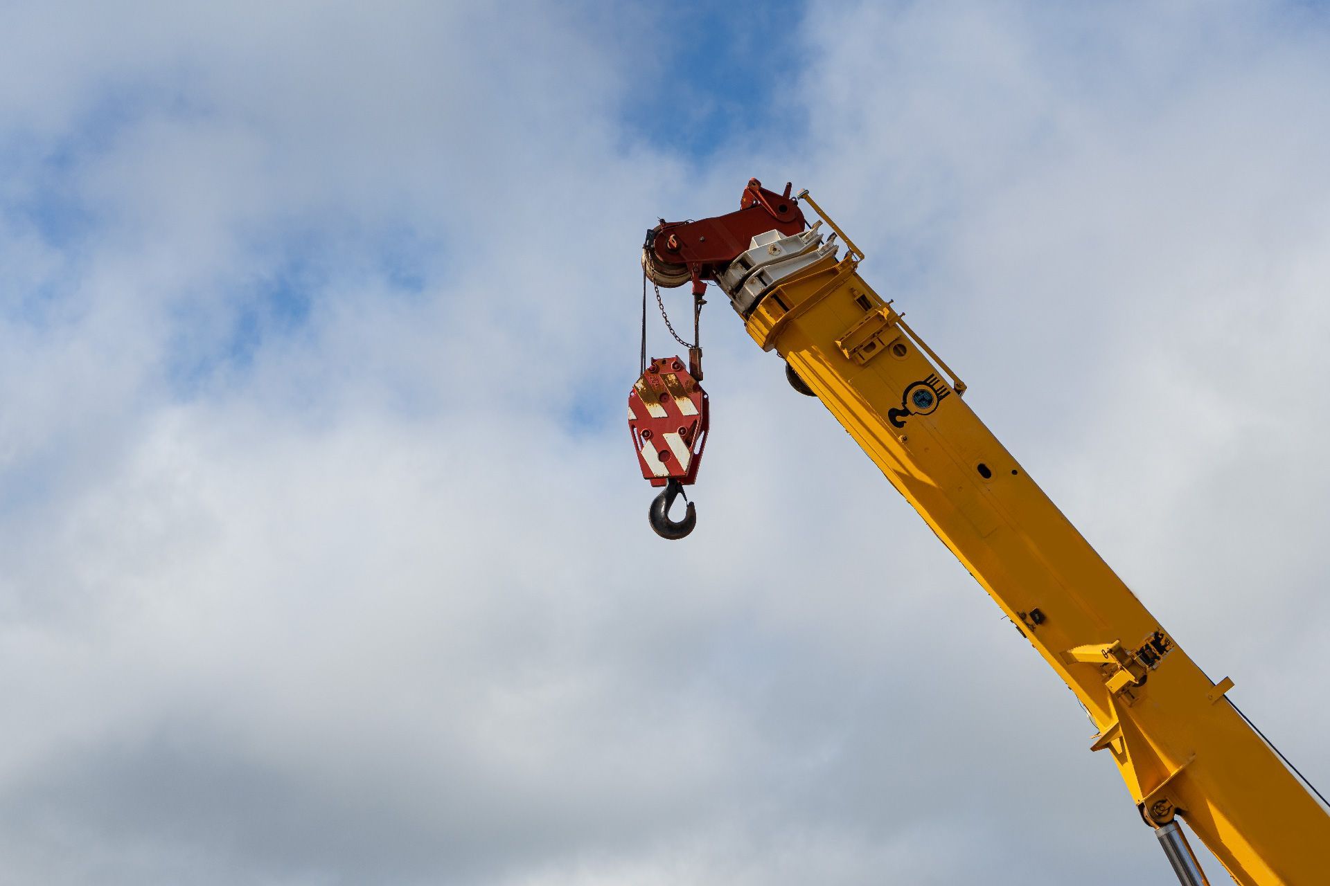 Brazo de grúa amarillo con gancho rojo contra un cielo nublado.