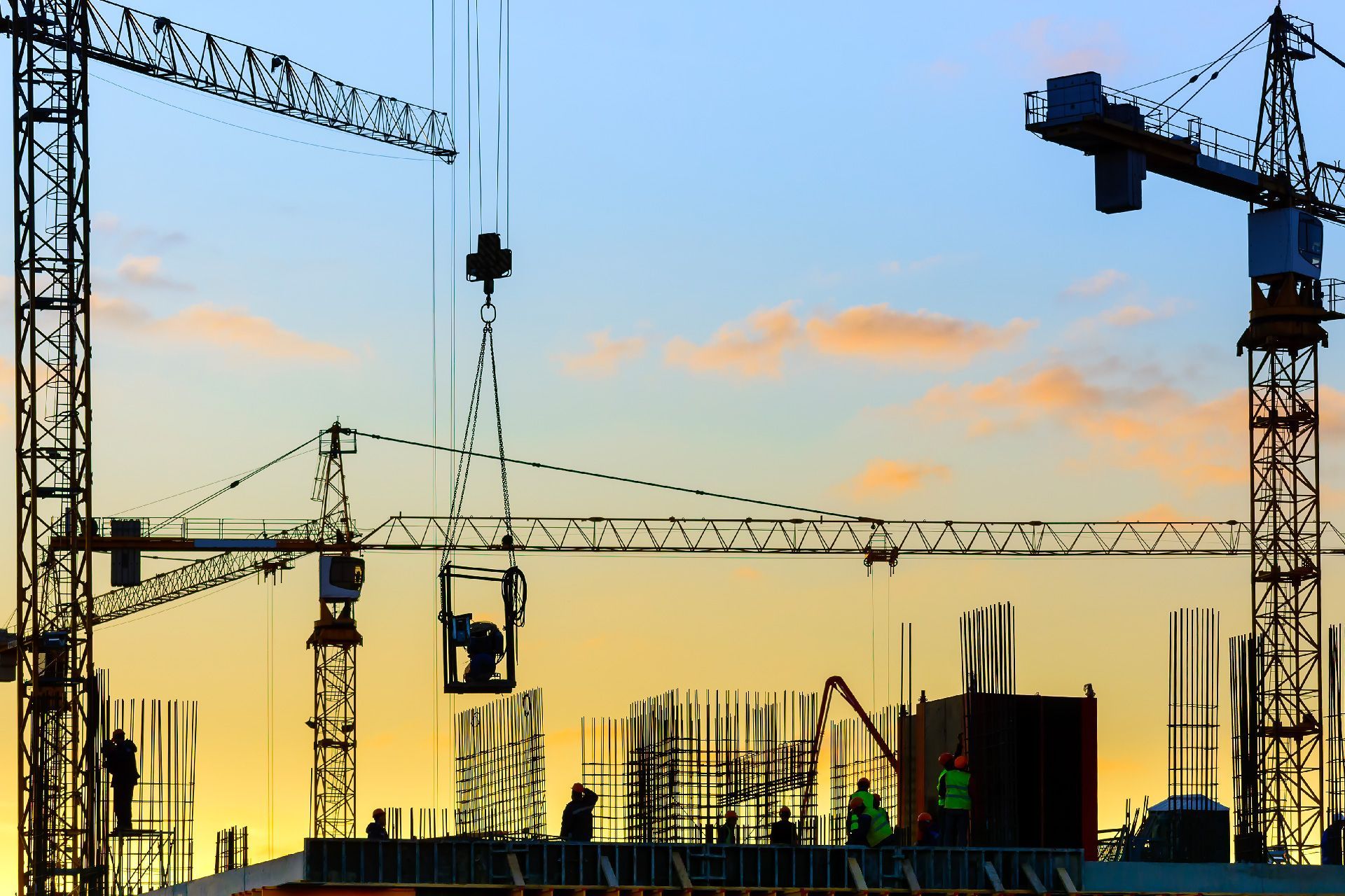 Obra de construcción con grúas recortadas contra un colorido atardecer. Trabajadores en la estructura de un edificio.