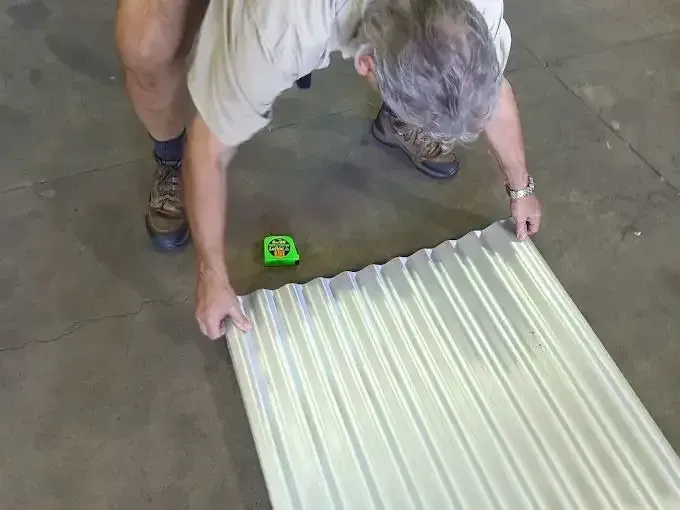 A Man Is Measuring A Piece Of Corrugated Metal With A Tape Measure — Colonial Sheet Metal in Garbutt, QLD