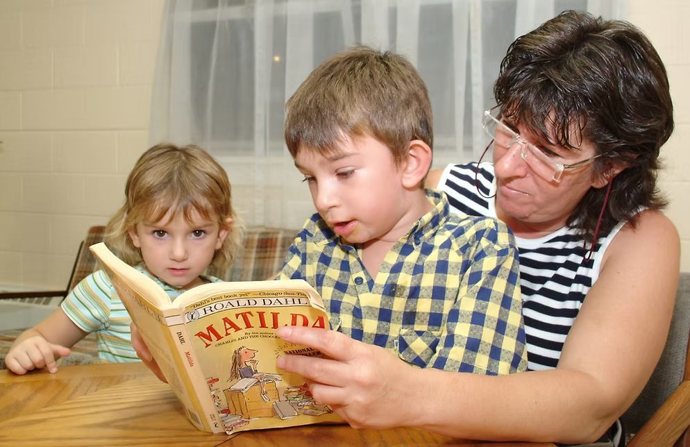Woman reads aloud to two children from "Matilda" book.