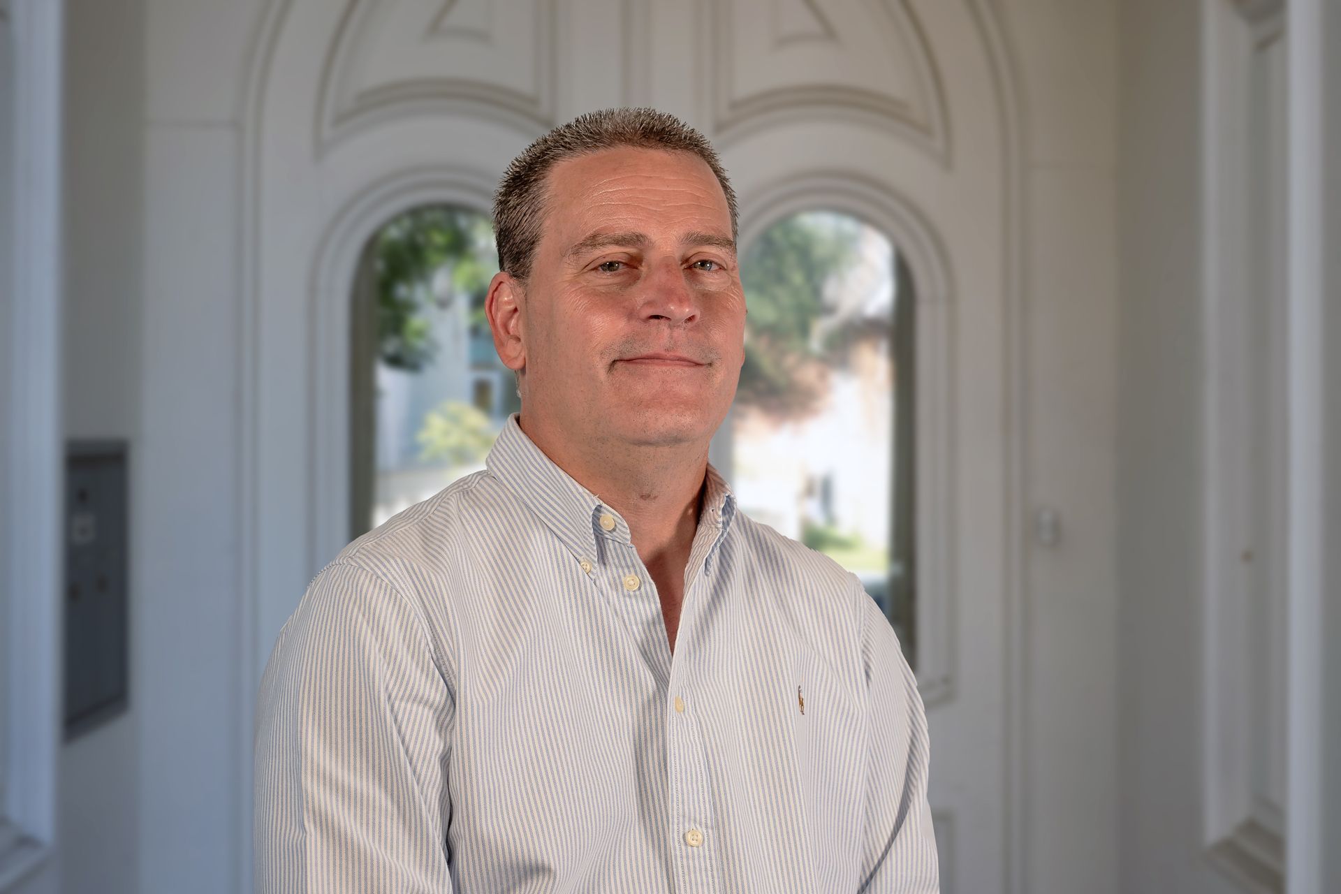 Man in light blue shirt smiles in front of white door.