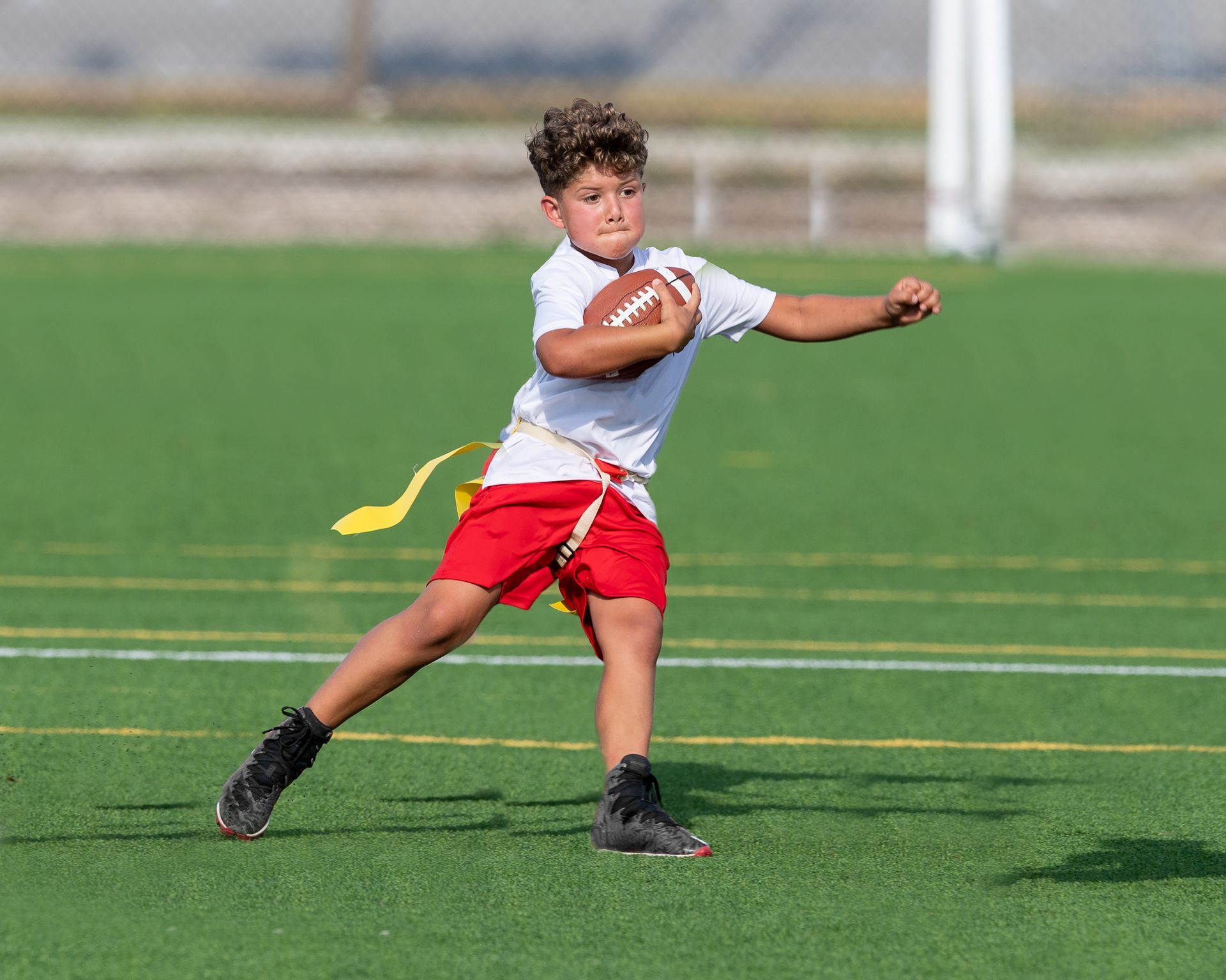Football players in action on a grassy field; one runs with the ball, pursued by two opponents.