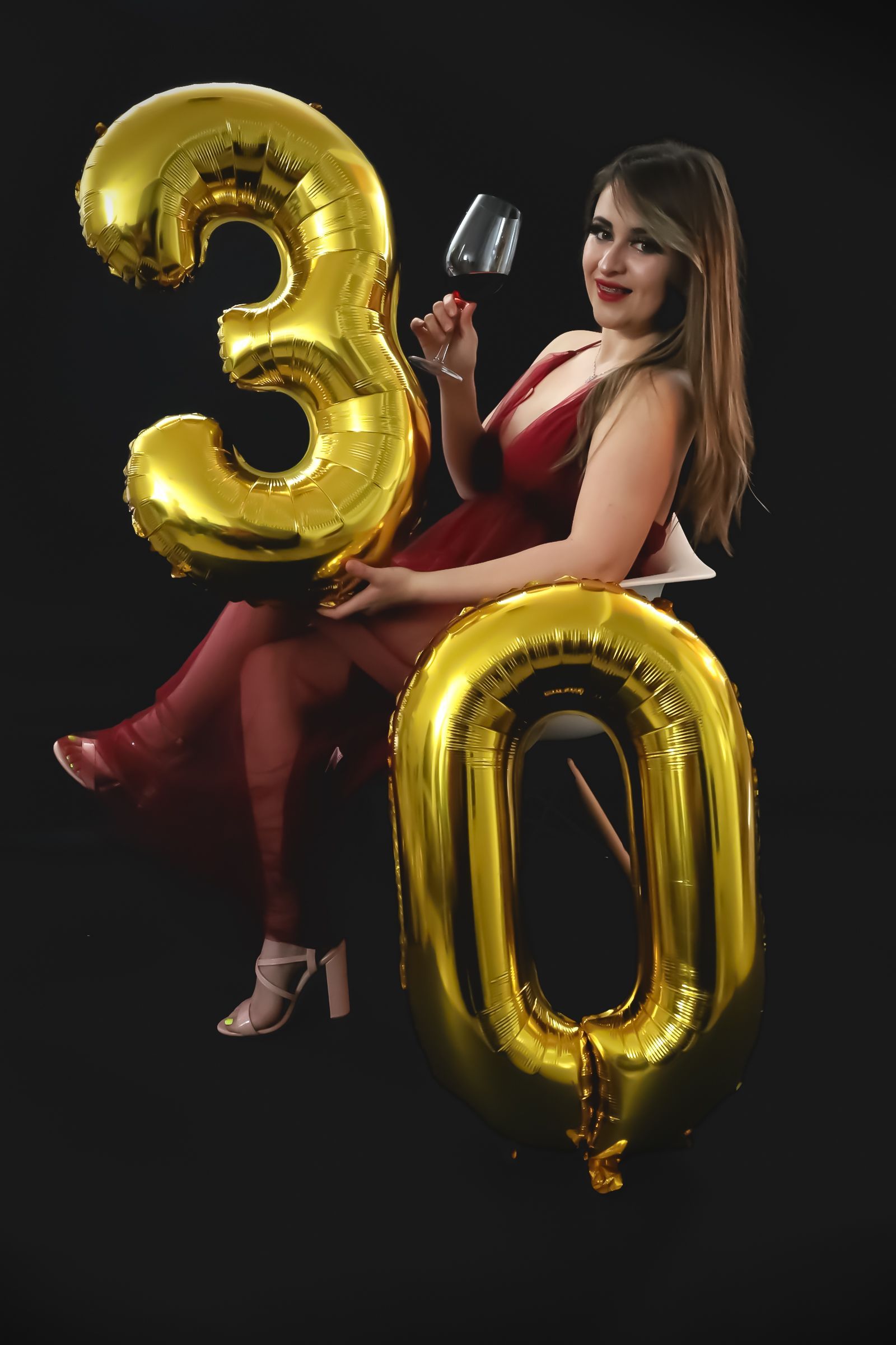 Une femme en robe rouge tient un verre de vin et des ballons en forme du numéro 30