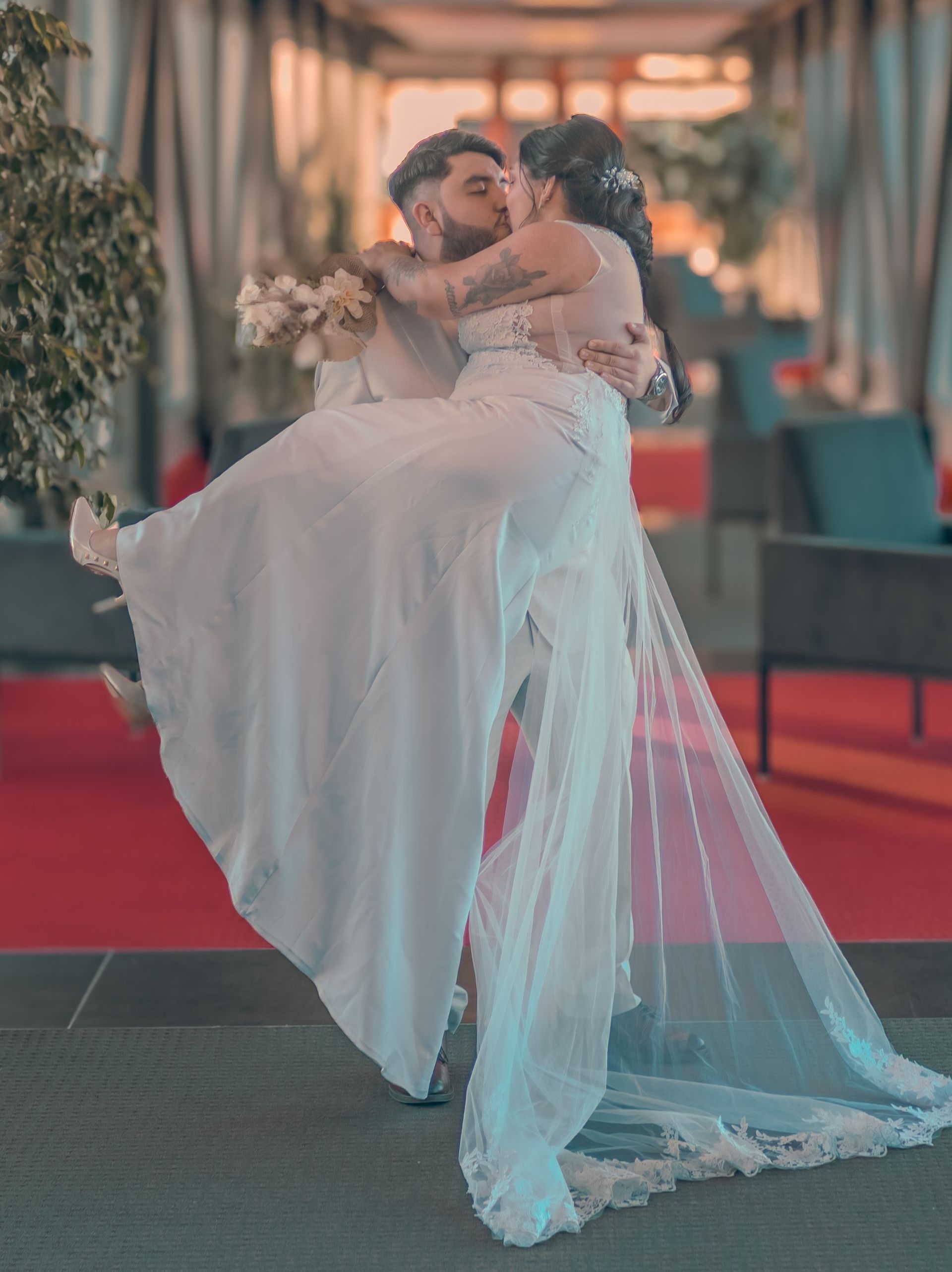 Les mariés s'embrassent passionnément ; le marié soulève la mariée dans les airs, dans un décor de mariage.