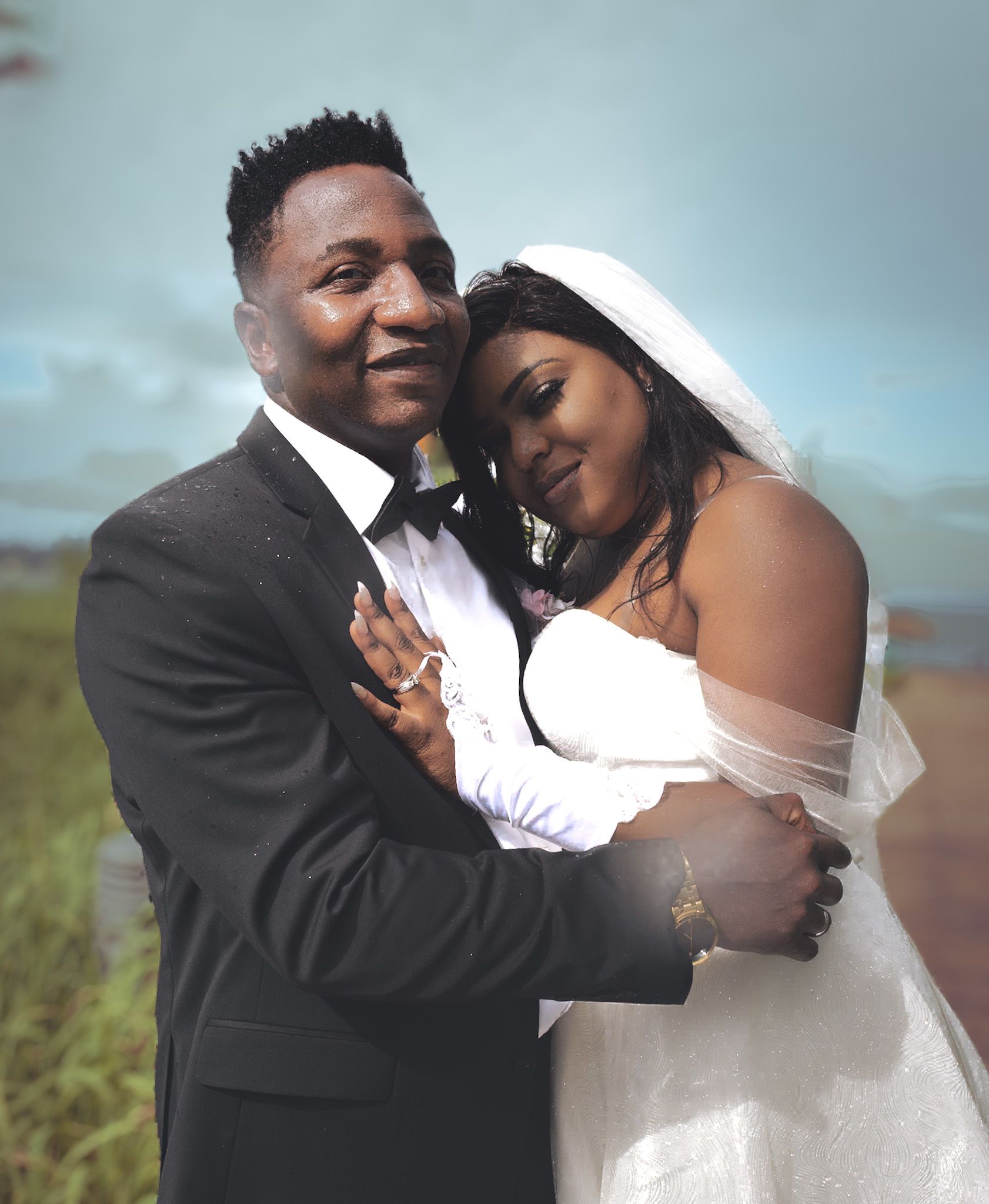 Couple de mariés enlacés : l'homme en costume et la femme en robe blanche, voilée. Décor extérieur.