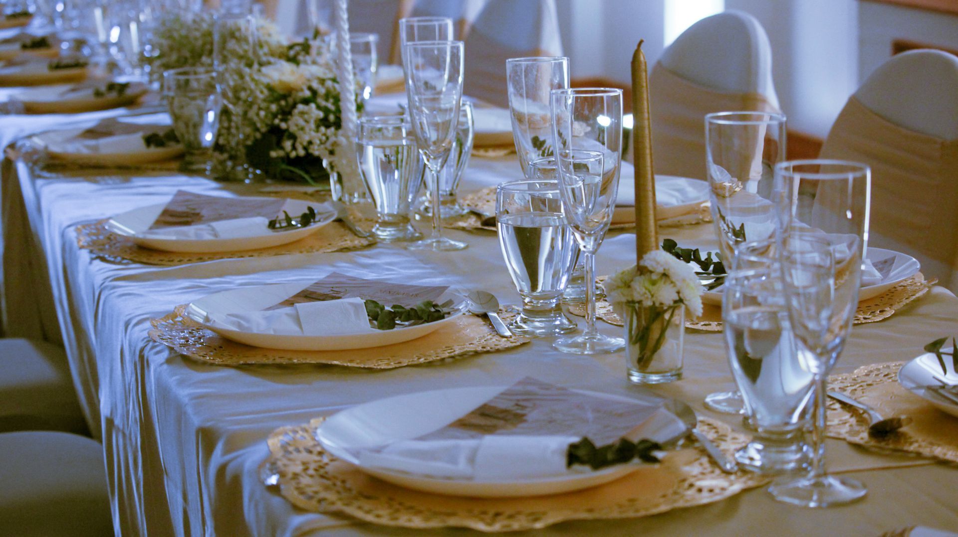 Une longue table dressée pour une réception de mariage avec des assiettes, des verres et des bougies.