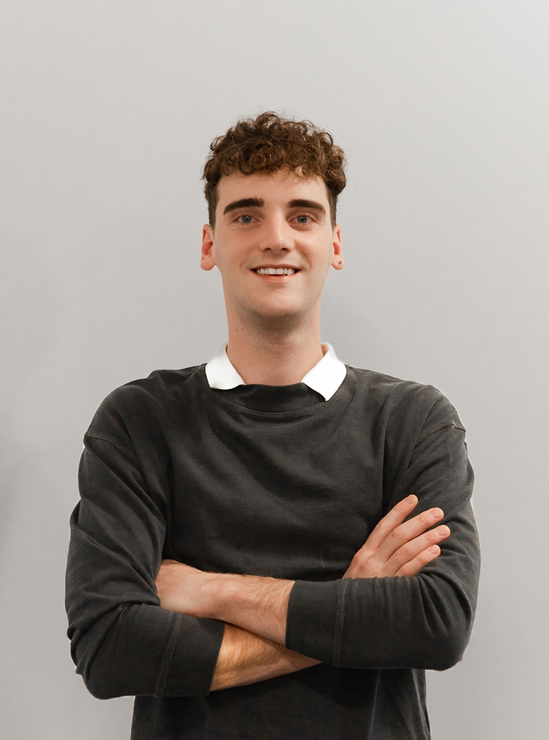 Un jeune homme est debout, les bras croisés et souriant.