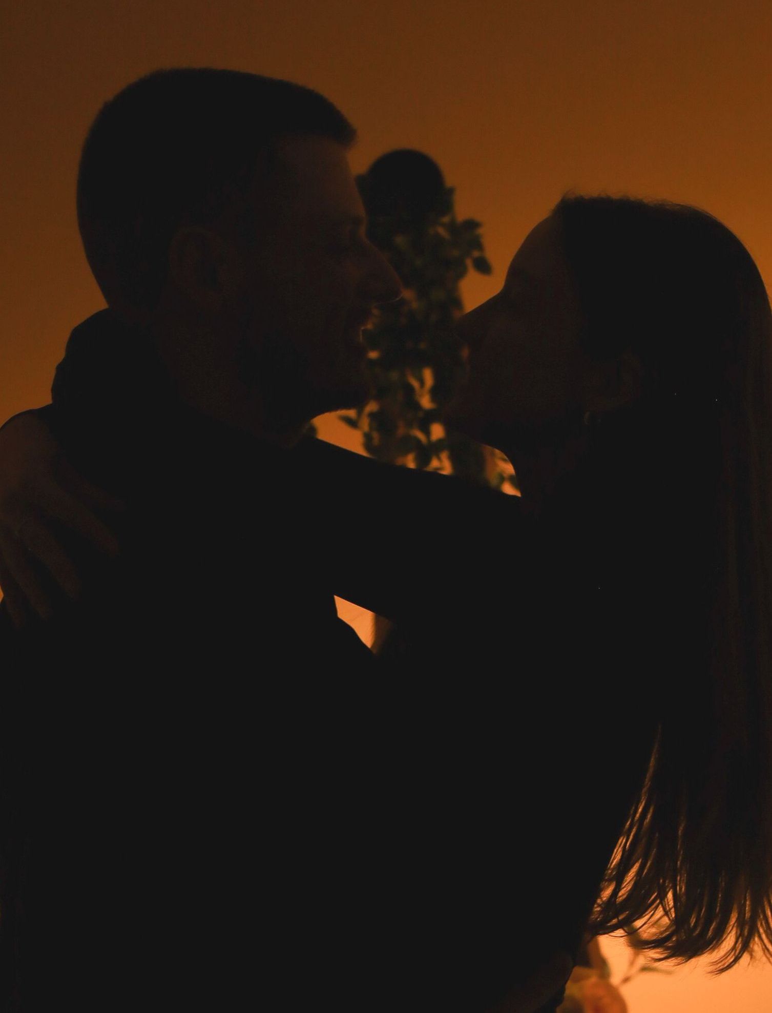 Couple en silhouette s'embrassant, éclairage chaleureux, enlacé.