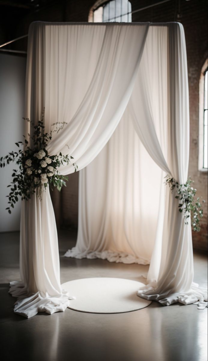Une arche de mariage décorée de rideaux blancs et de fleurs dans une pièce.