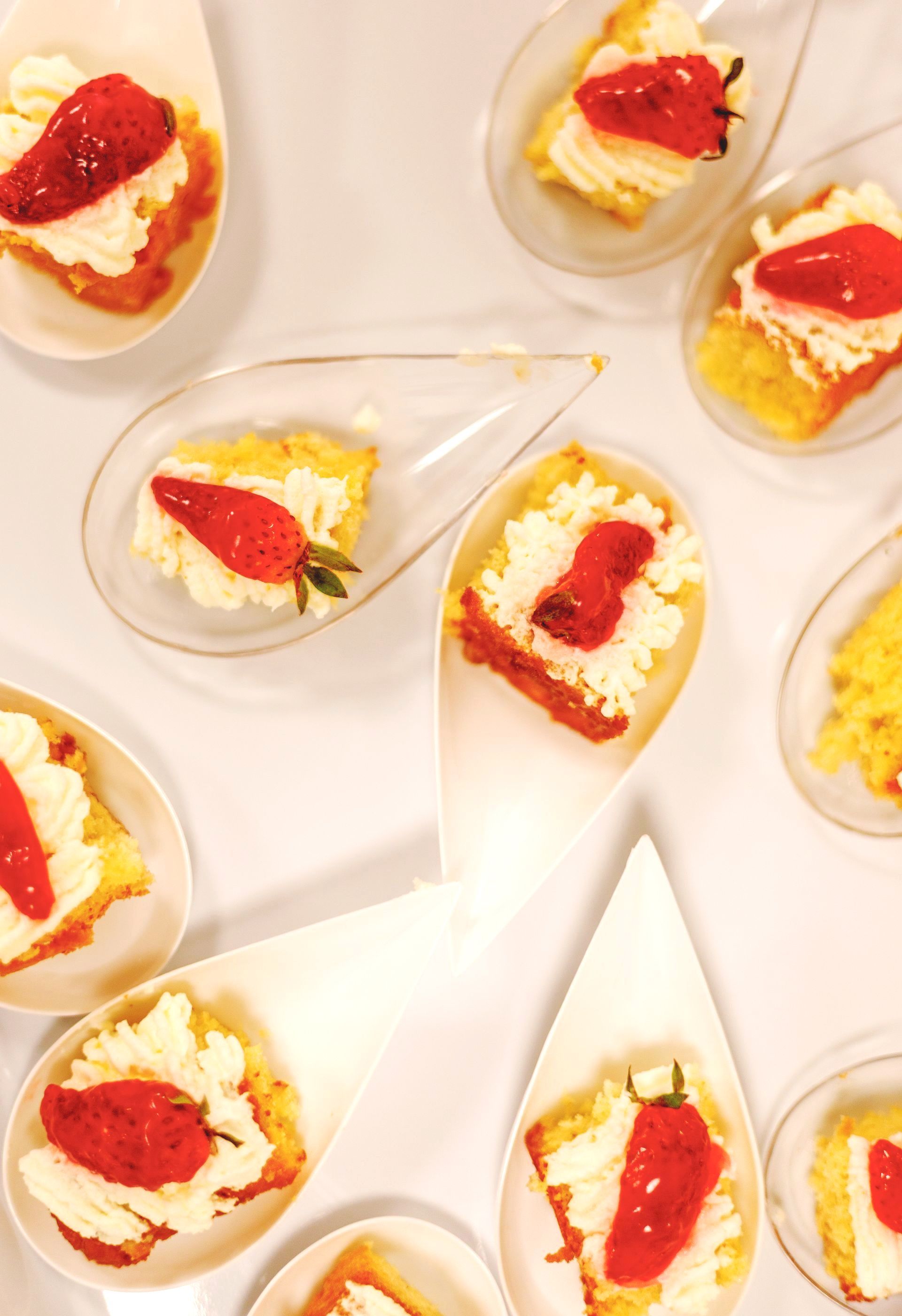 Petites bouchées de gâteau avec glaçage blanc et une moitié de fraise sur une surface blanche.