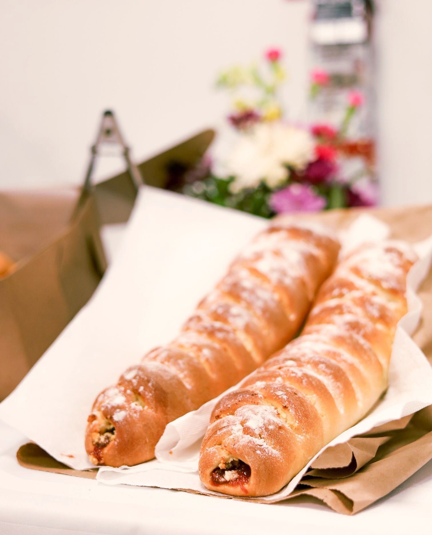 Deux pâtisseries cuites au four sur papier blanc, fond papier brun, fleurs au loin.