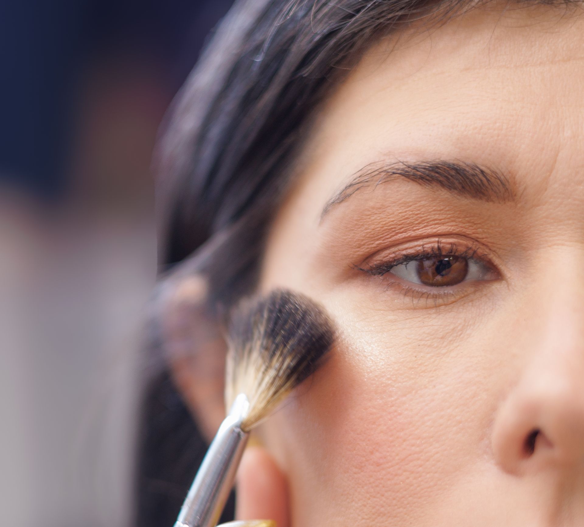 Application du blush sur les joues avec un pinceau à maquillage. Fard à paupières marron, yeux marron, teint neutre.