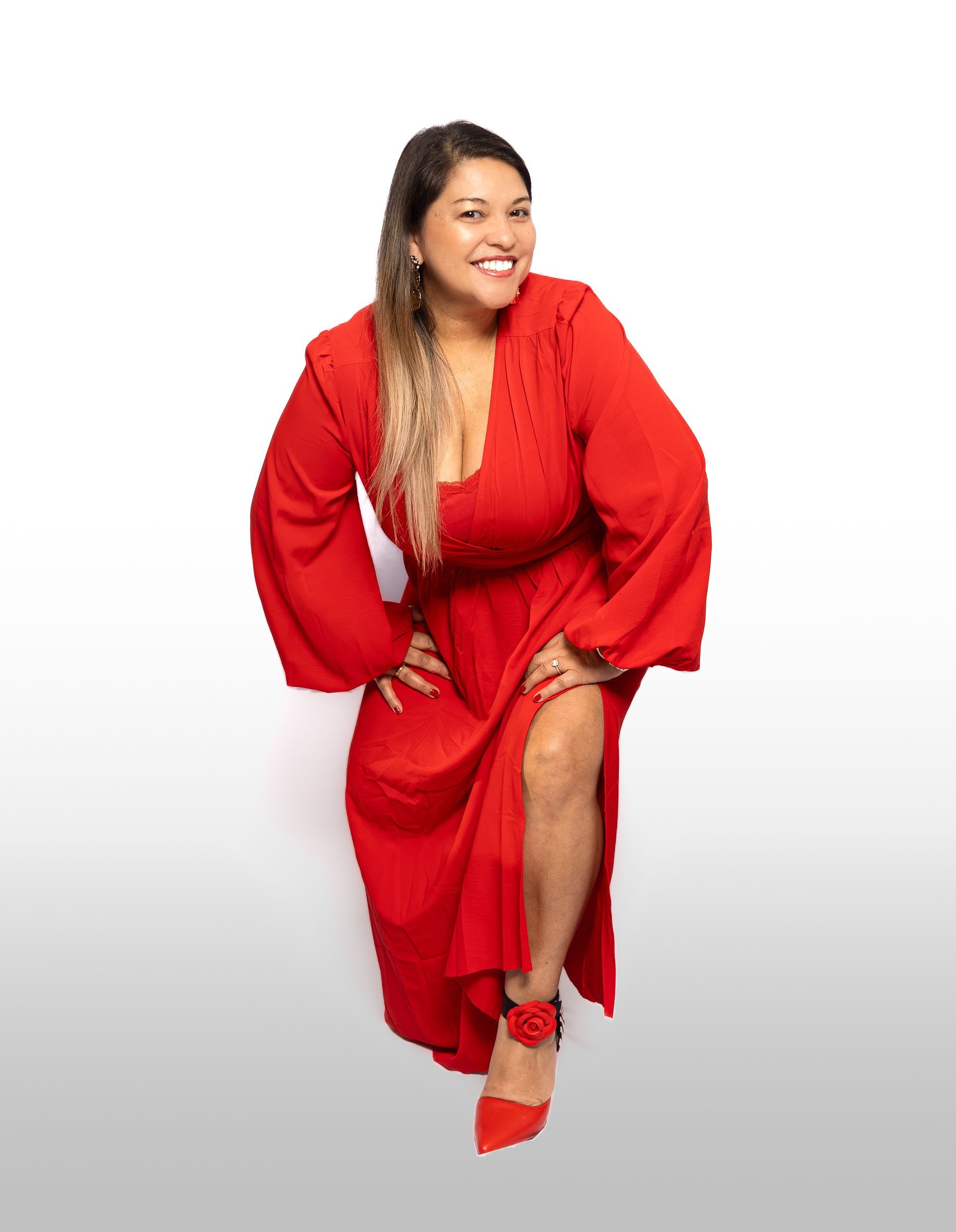 Femme souriante, vêtue d'une robe rouge fendue jusqu'à la cuisse, posant avec une main sur la hanche, chaussures rouges.