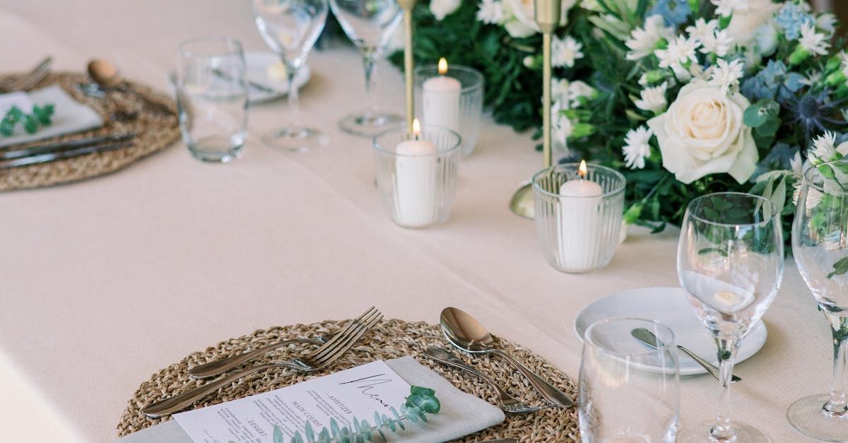 Une table dressée pour une réception de mariage avec assiettes, verres à vin, bougies et fleurs.
