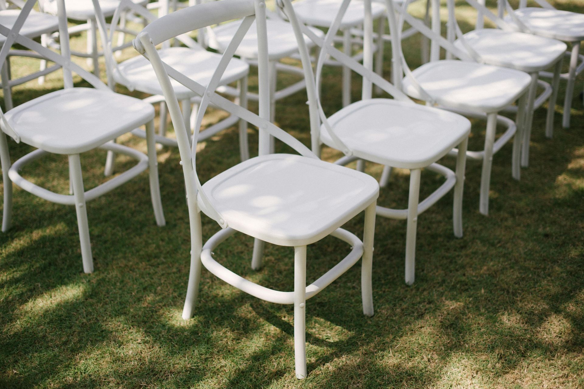 Des rangées de chaises blanches à dossier croisé disposées sur la pelouse, dans un jardin.