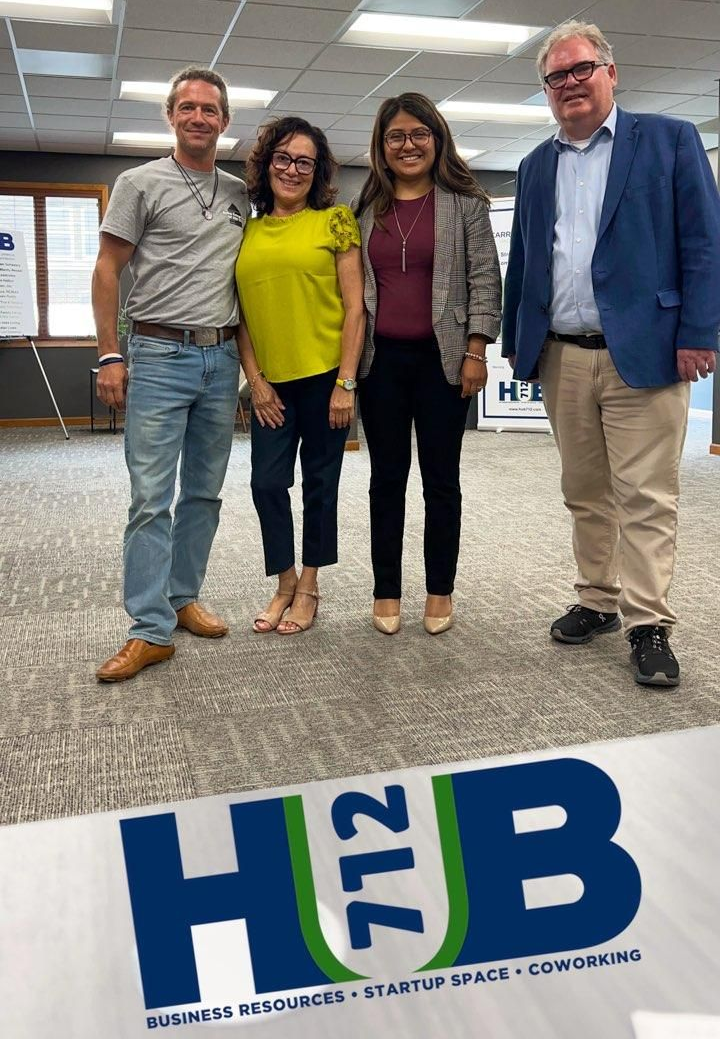 Four people standing in front of a logo. Two women and two men smiling inside an office. The logo reads