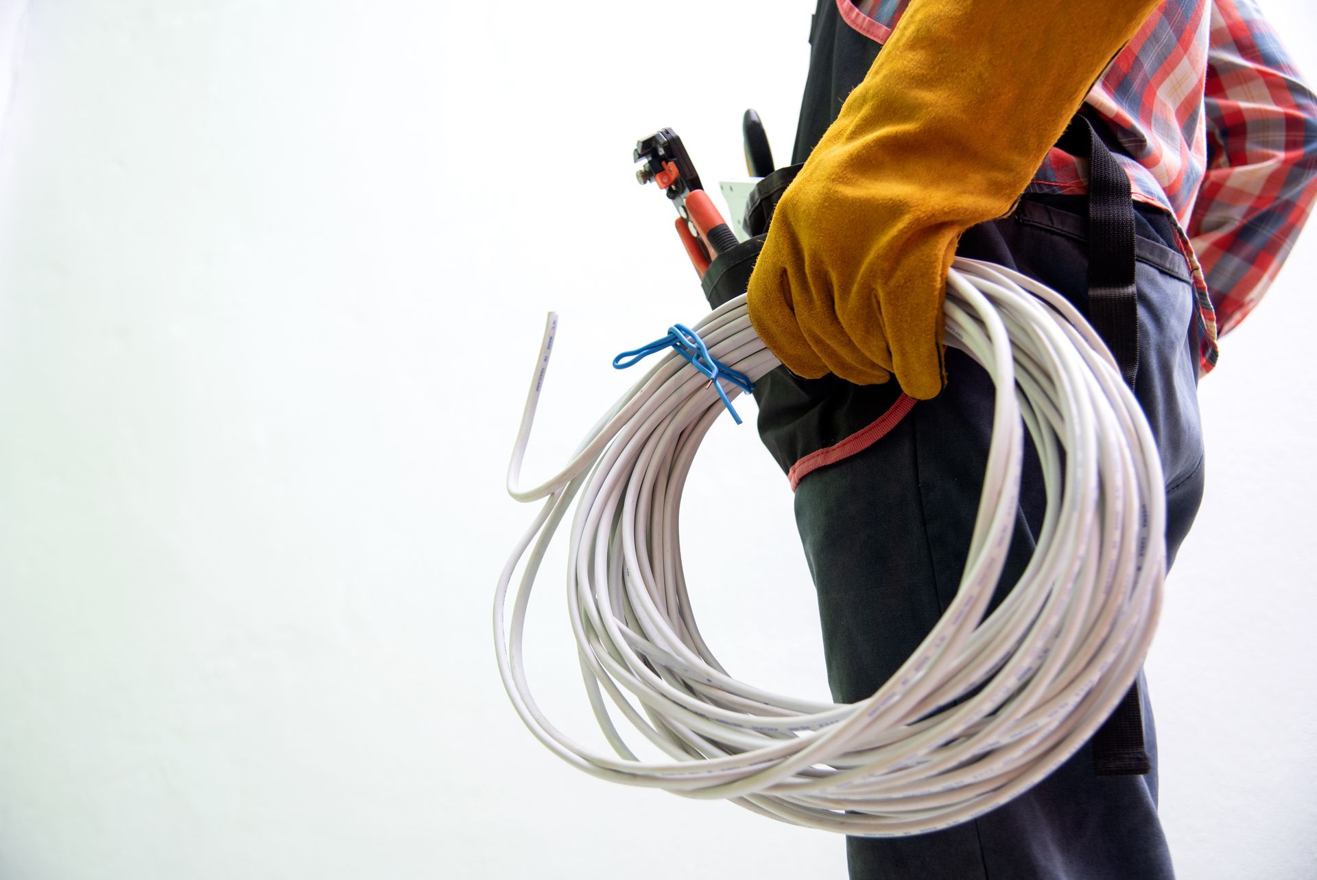Worker holding a coiled electrical cable with tools in a belt. Worker holding a coiled electrical cable with tools in a belt.