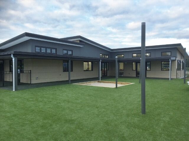 A light gray, single-story building with a dark roof and a large grassy courtyard.