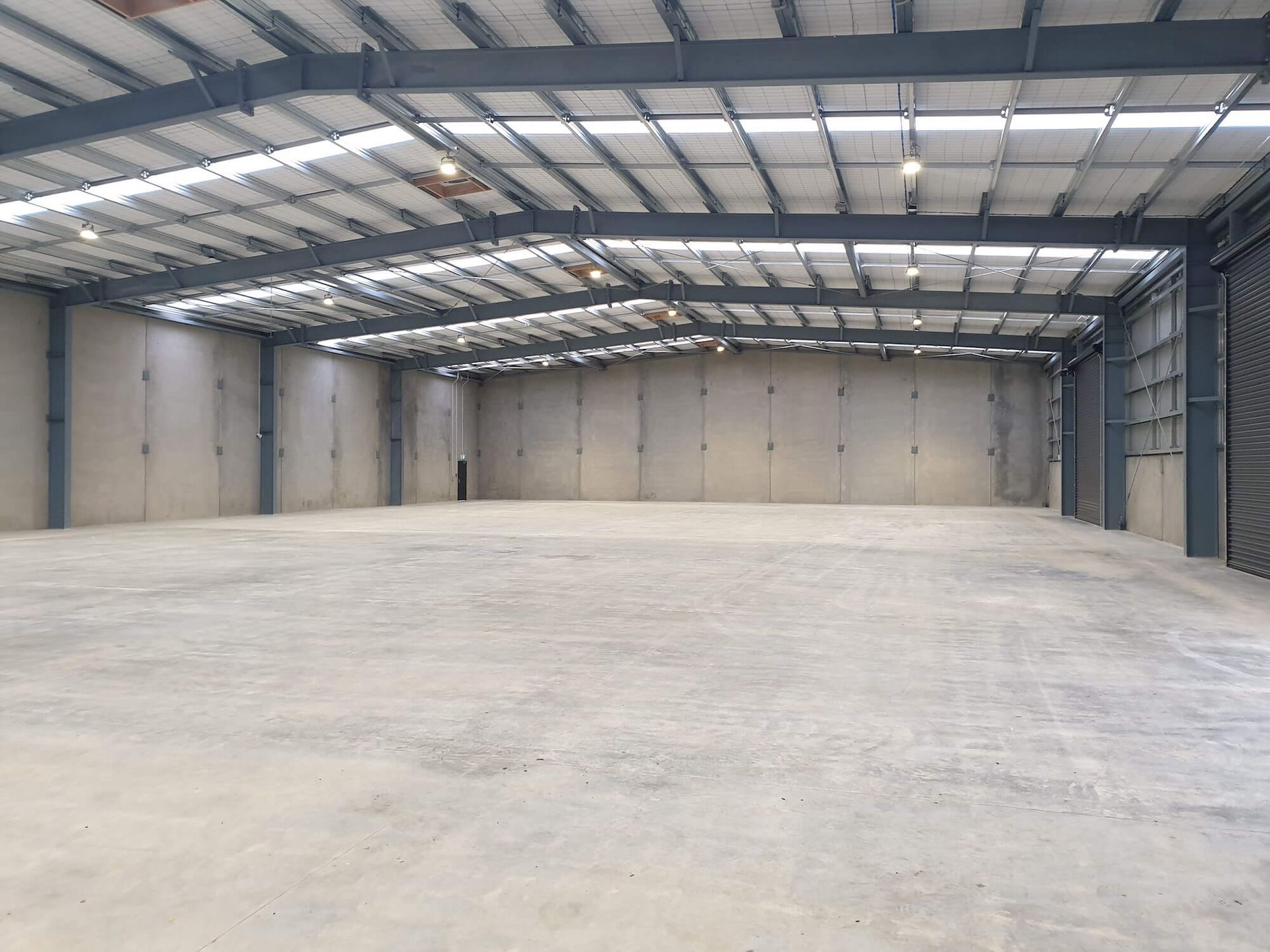 Empty warehouse interior with gray concrete walls and floor, metal beams, and open ceiling.