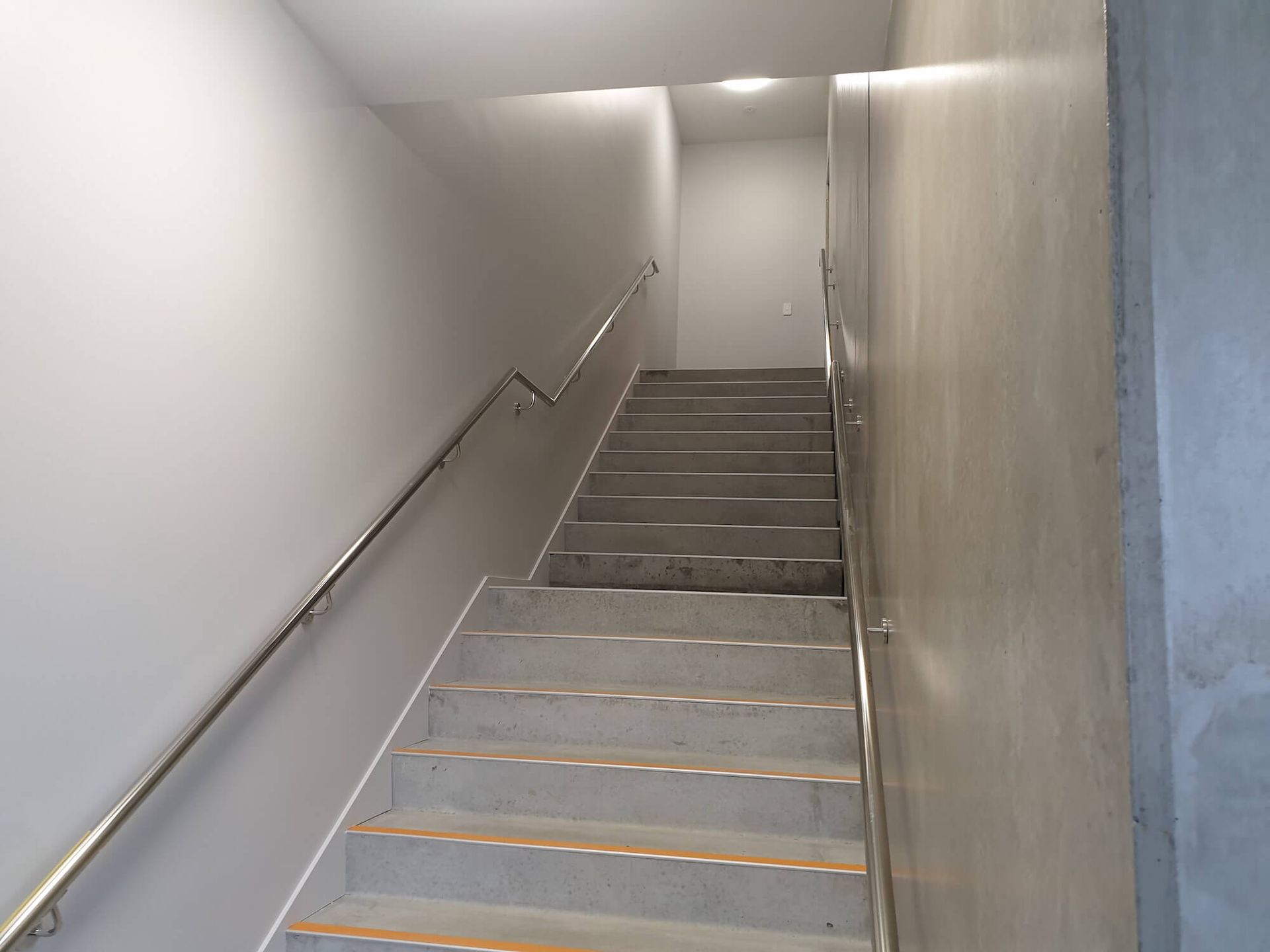 Staircase ascending between gray walls, metal handrails on either side.