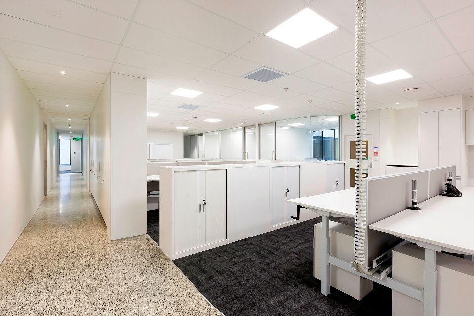 Office space with rows of white cubicles, white desks, and a hallway with a textured floor.