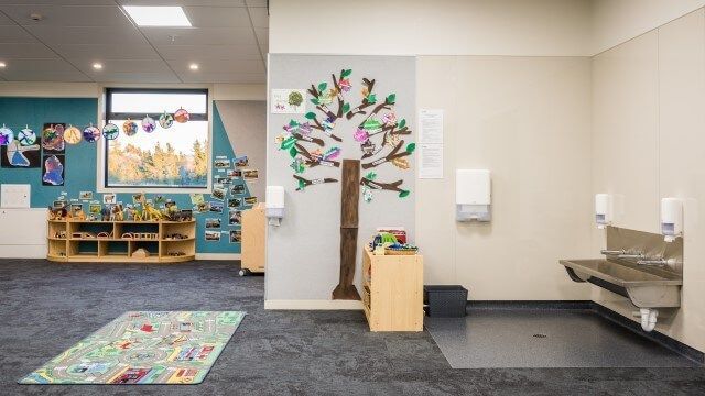 Kindergarten classroom with a tree mural on a wall, a rug, and a sink.