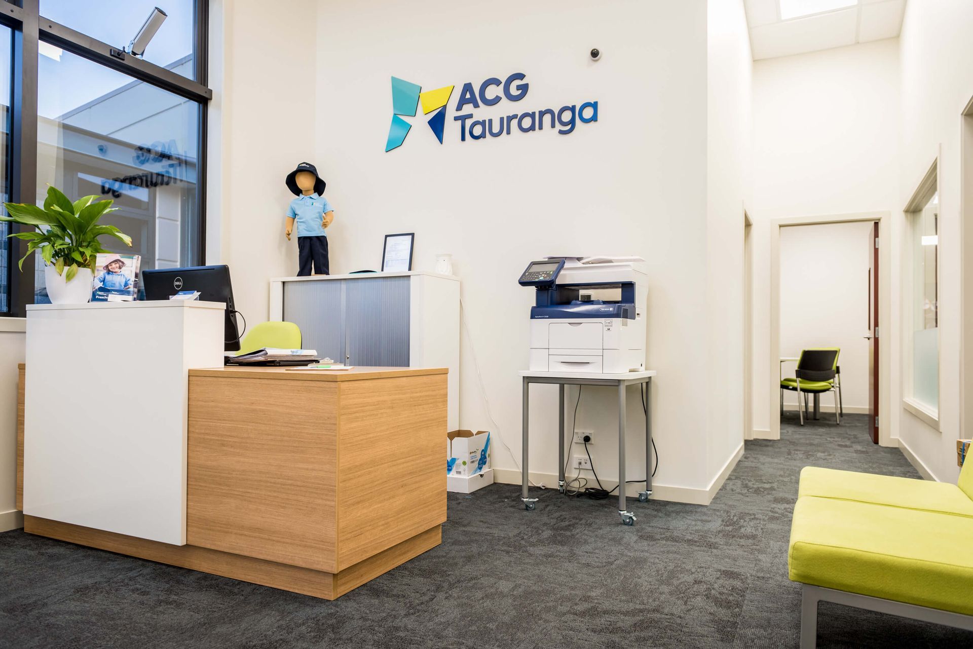 Reception area at ACG Tauranga. A wooden and white desk sits at the front. The ACG Tauranga logo is above.