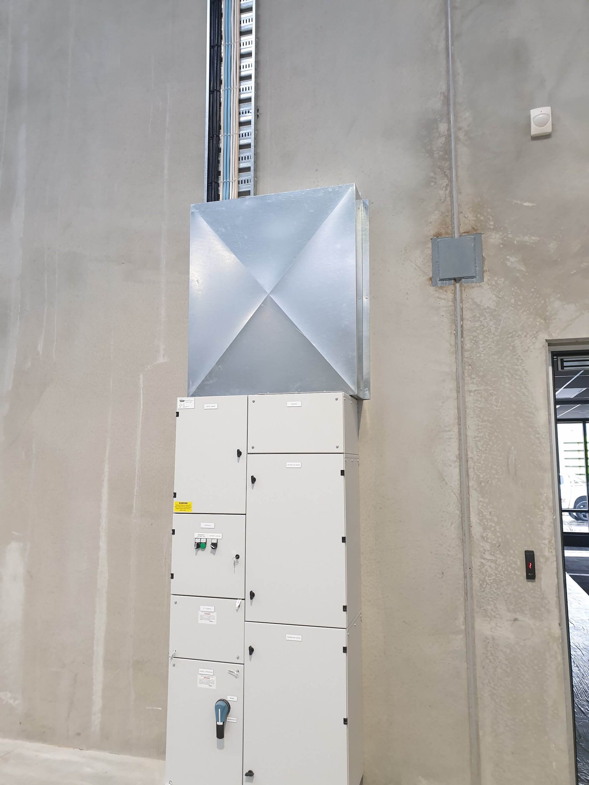 An electrical panel with a metal vent cap mounted on a concrete wall.