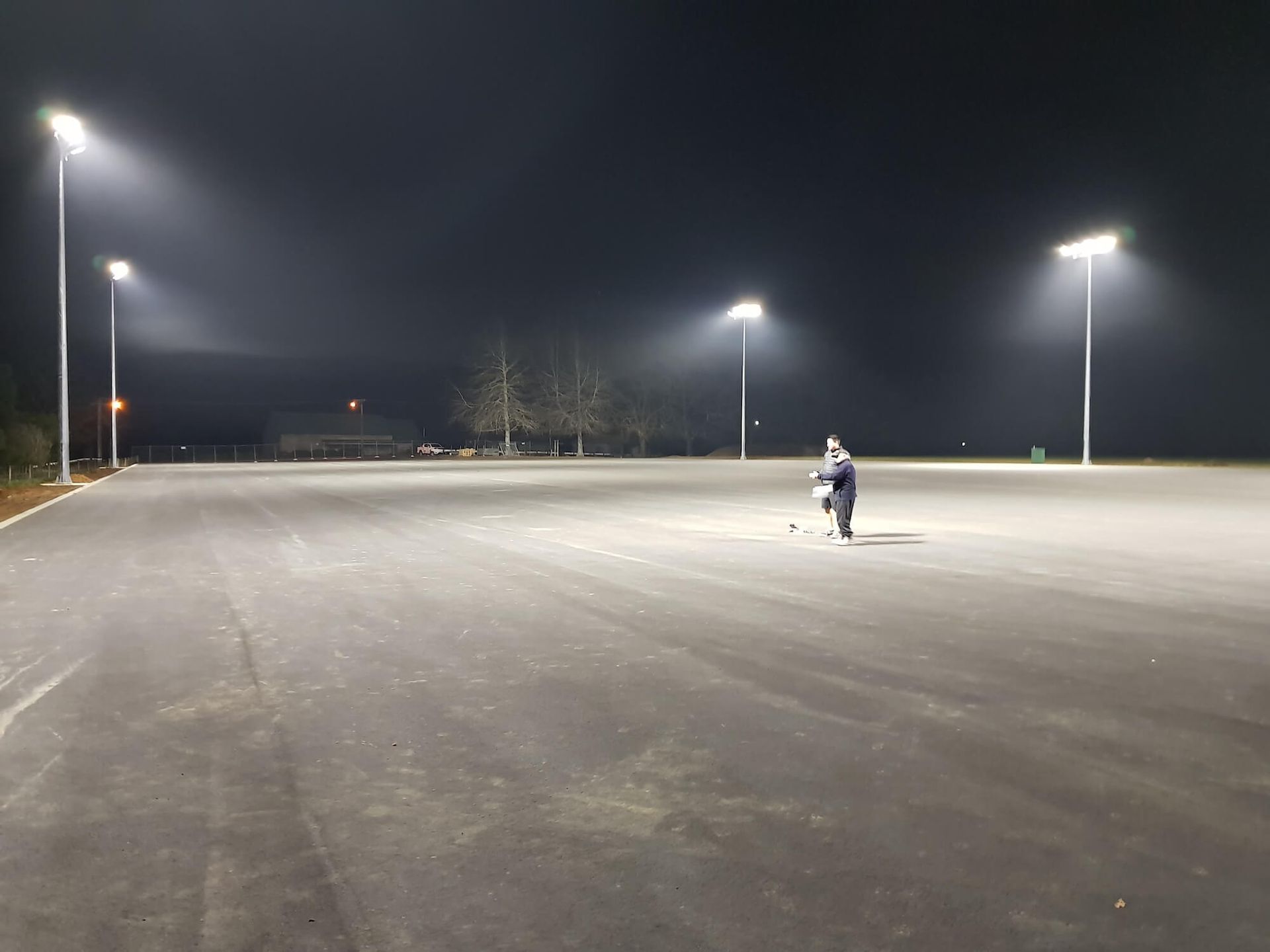A person stands on an empty, dark asphalt lot illuminated by streetlights at night.
