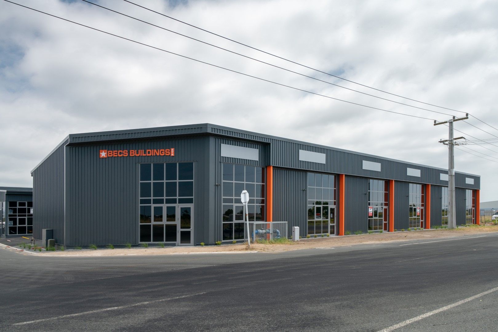 Dark gray industrial building with orange accents, located on a street under a cloudy sky.