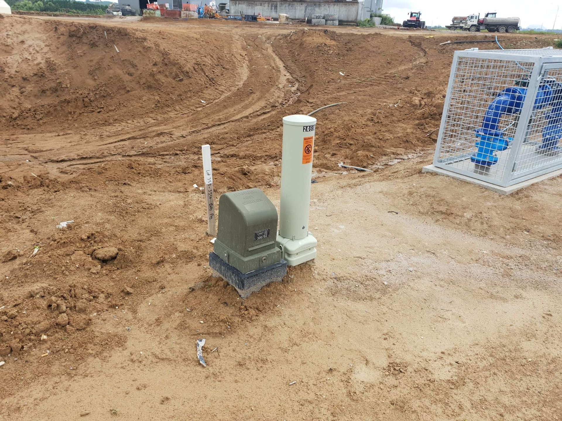 Dirt construction site, utility box with a tall, white marker, and a caged water valve.