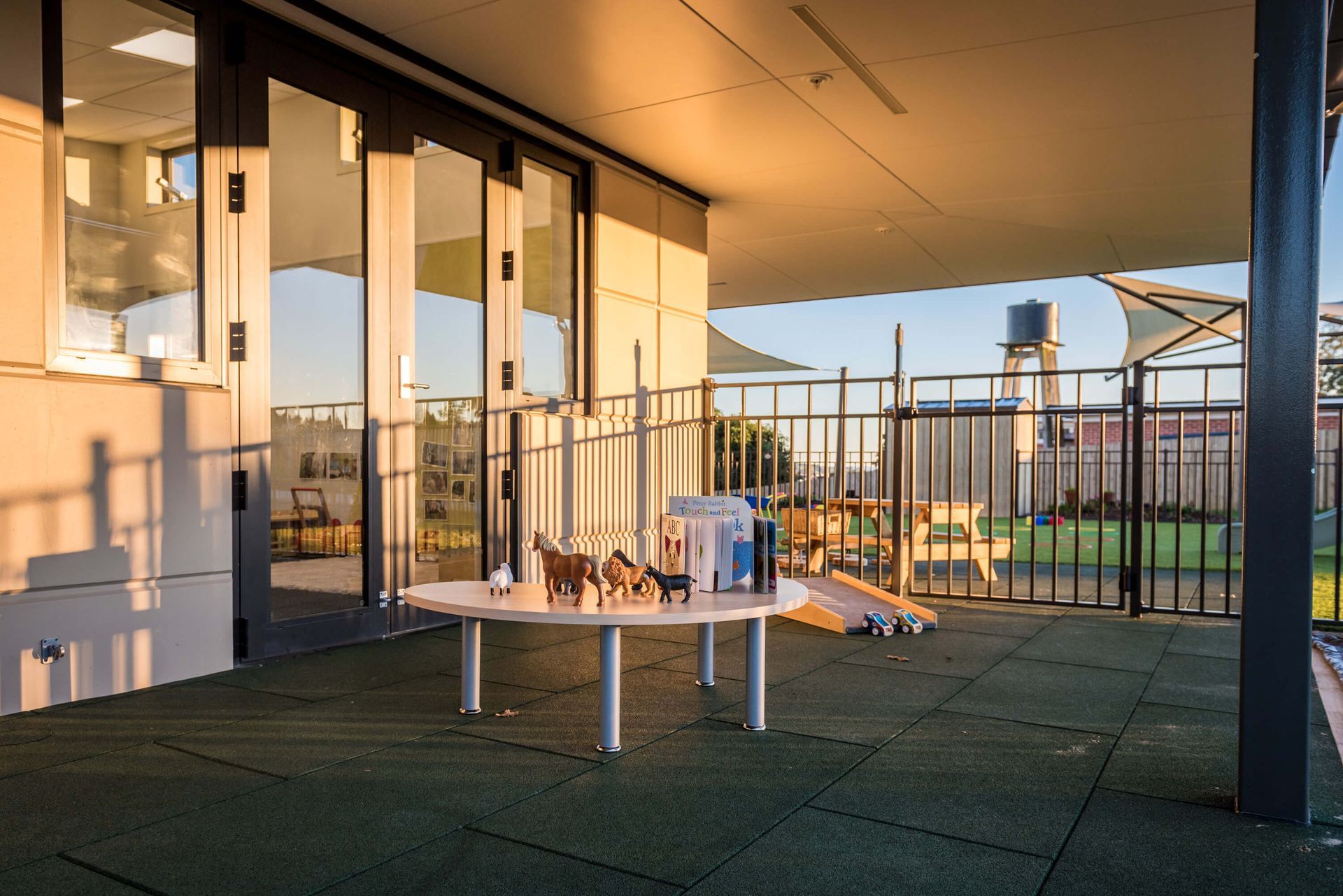 Outdoor play area with a table, books, and toys; a slide and fenced area are visible.