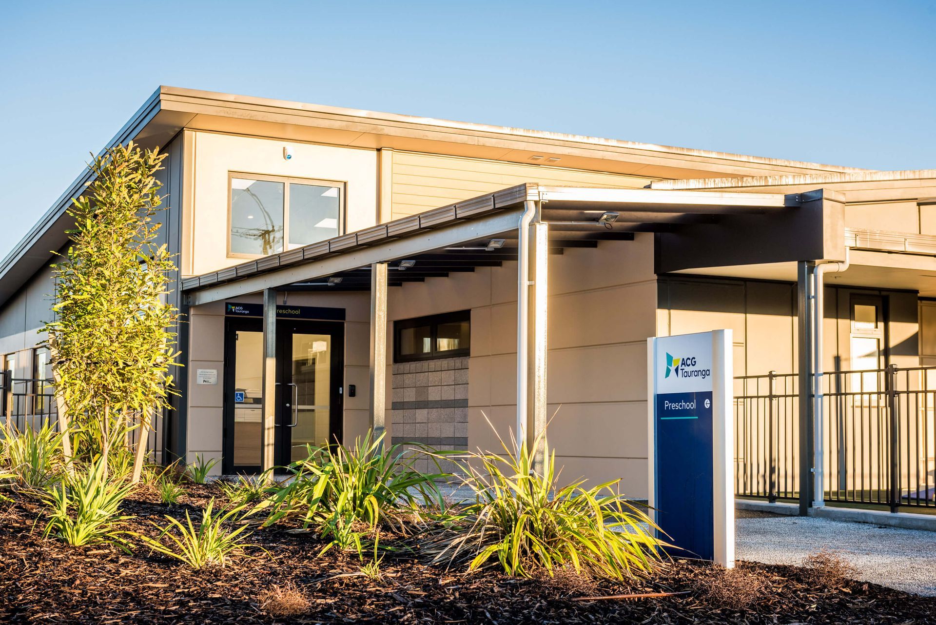 Modern, one-story building with a shaded entryway and a sign, set against a sunny backdrop.