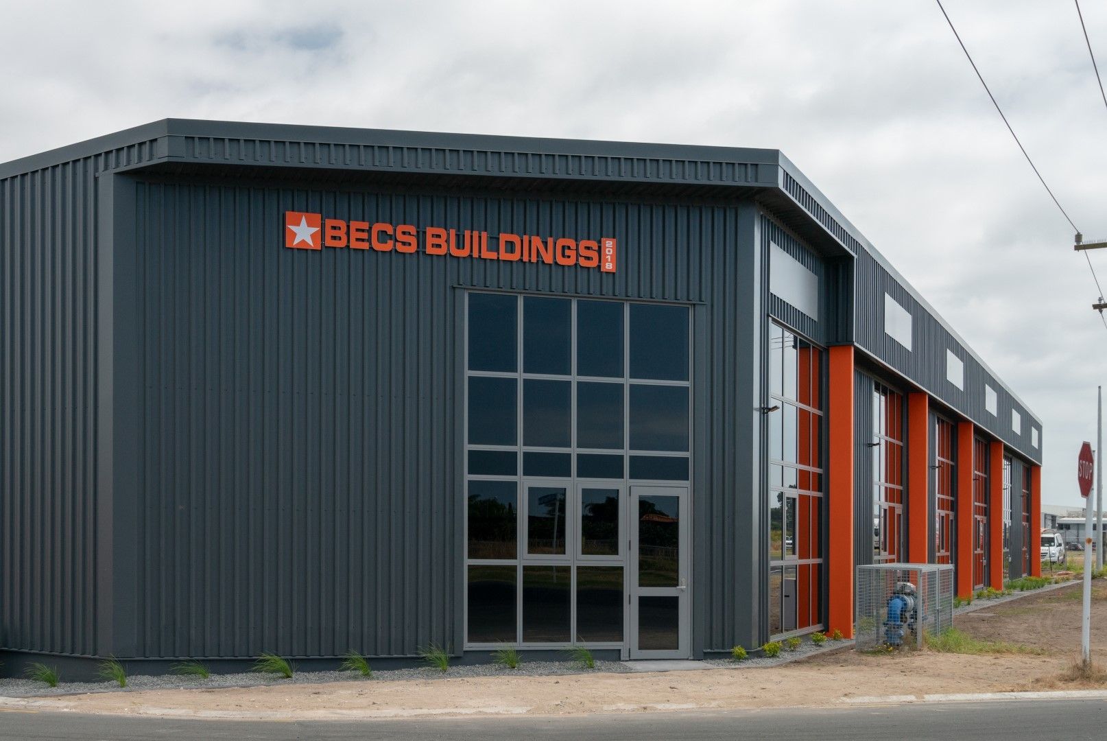 Exterior of BECS Buildings, a modern industrial-style building with gray siding and orange accents. A sign displays the company name.