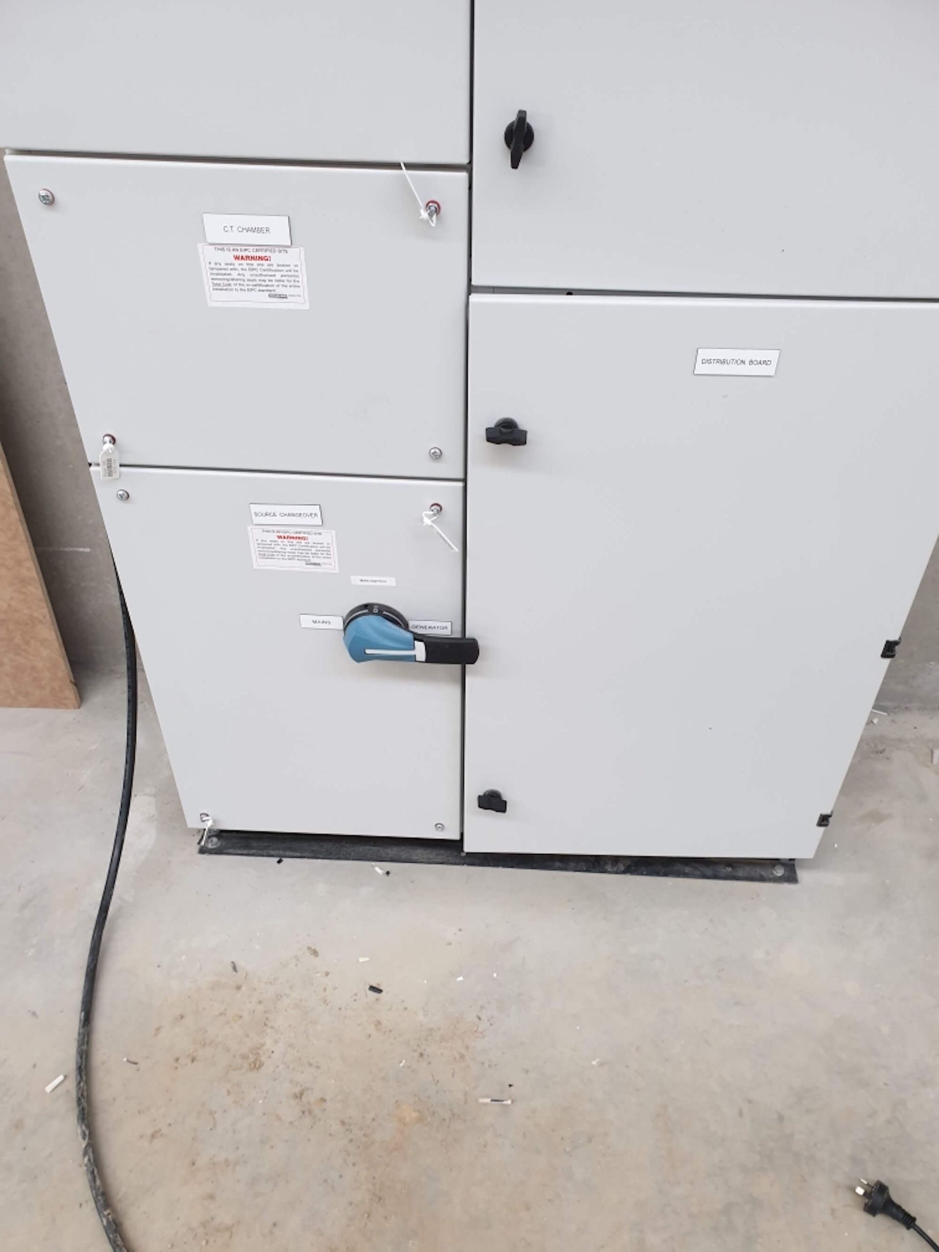 Electrical control panel with various gray doors and black handles; a large black cable is visible.