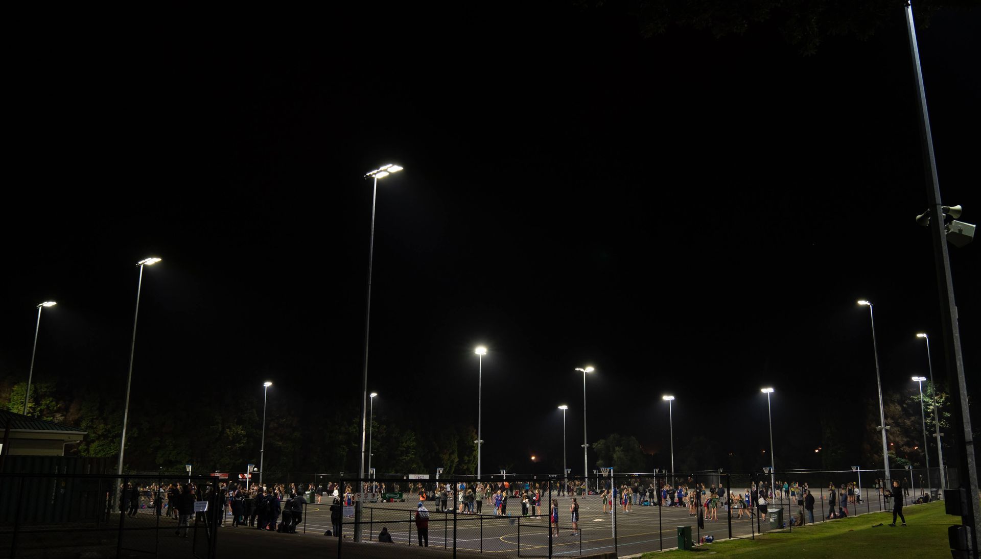 A night view of a large lit sports field with many people, under tall streetlights.