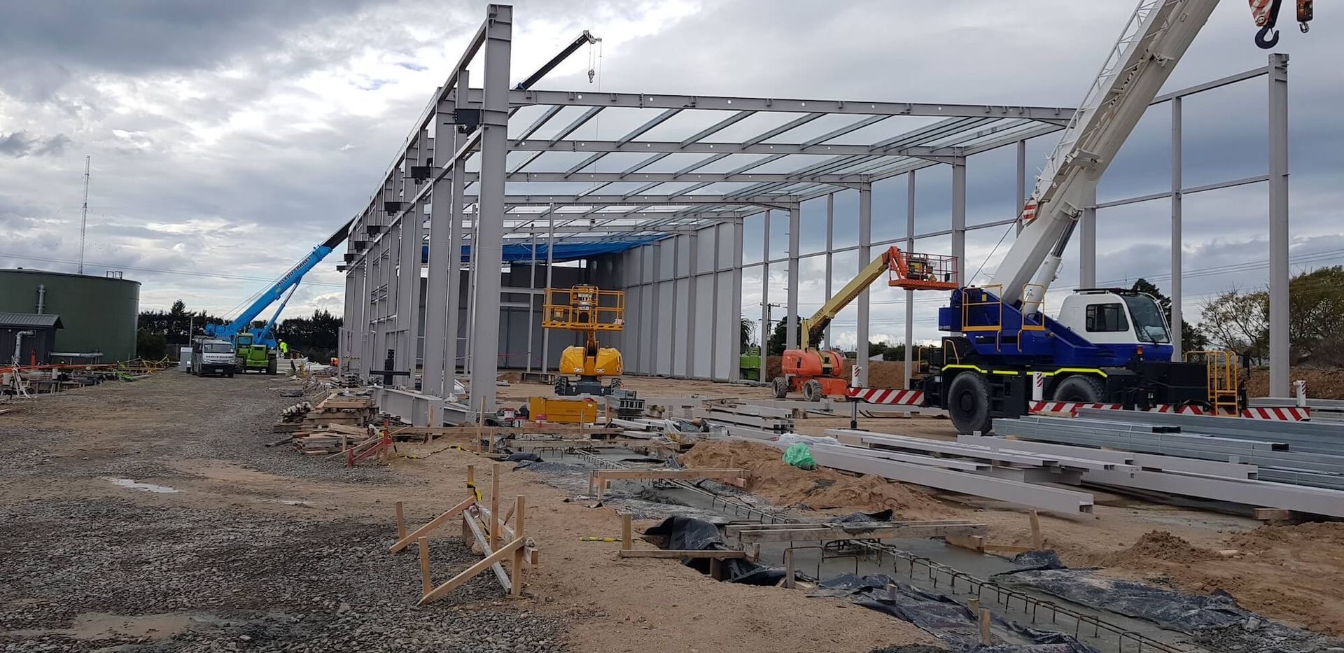 Construction site with a steel frame building under construction. Cranes and other heavy machinery are present. Construction site with a steel frame building under construction. Cranes and other heavy machinery are present.