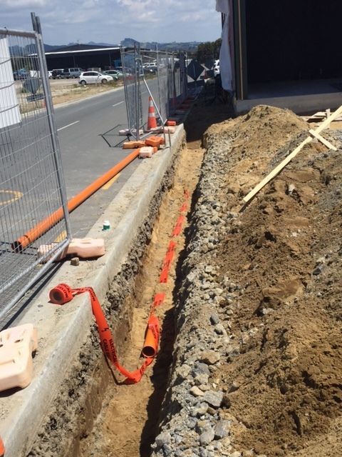 A trench dug for utility lines next to a road, with orange conduit and protective barriers.