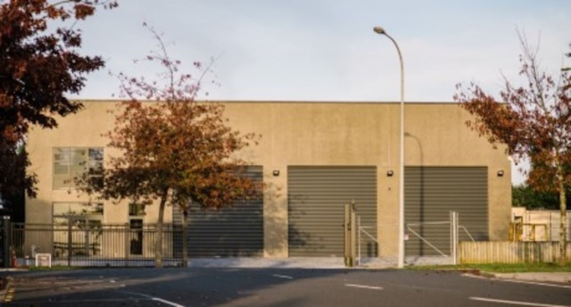 Exterior of a neutral-toned industrial building with two garage doors and a window. A tree with red leaves stands in front.