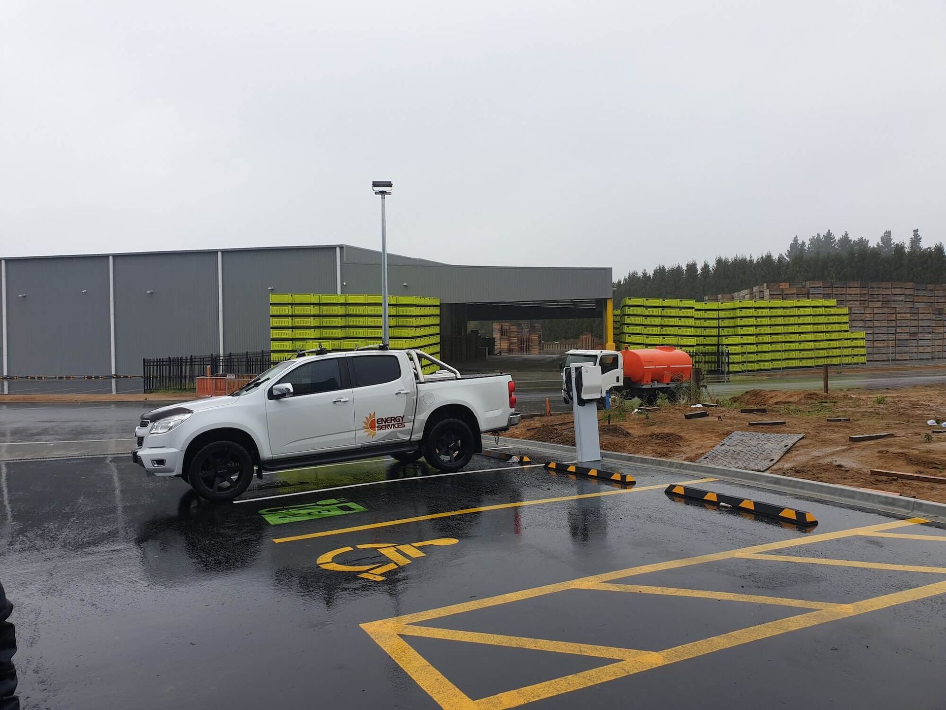 White truck parked at an accessible charging station near a building under construction. Wet asphalt, overcast day.