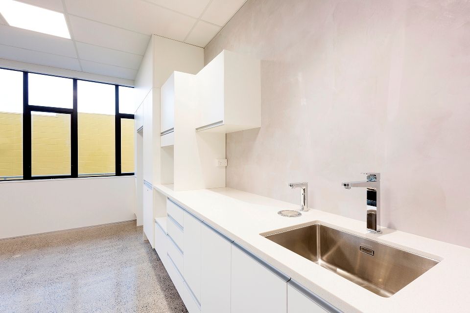 Modern white medical office with a sink, cabinets, and a window with a yellow blind.