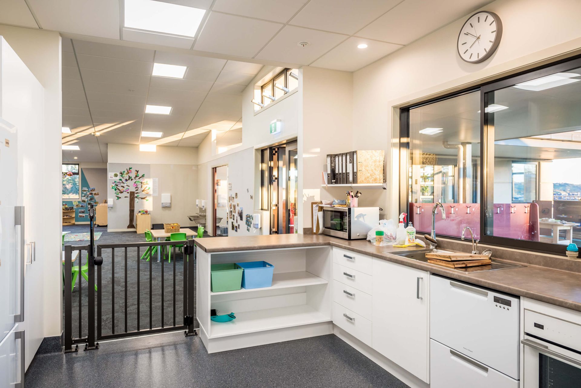 A modern, bright preschool kitchen. White cabinets and countertops, with a sink, microwave, and small appliances.