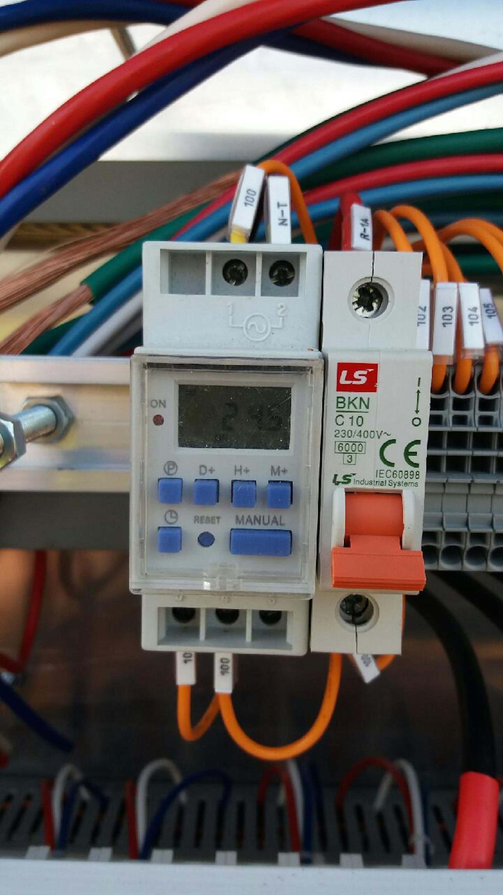 Close-up of electrical panel components including a digital timer, circuit breaker, and wires of various colors.