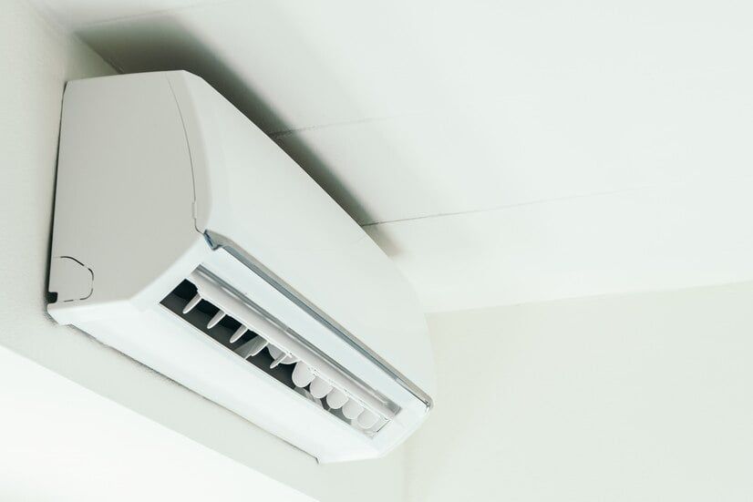White wall-mounted air conditioner on a white wall, blowing air.