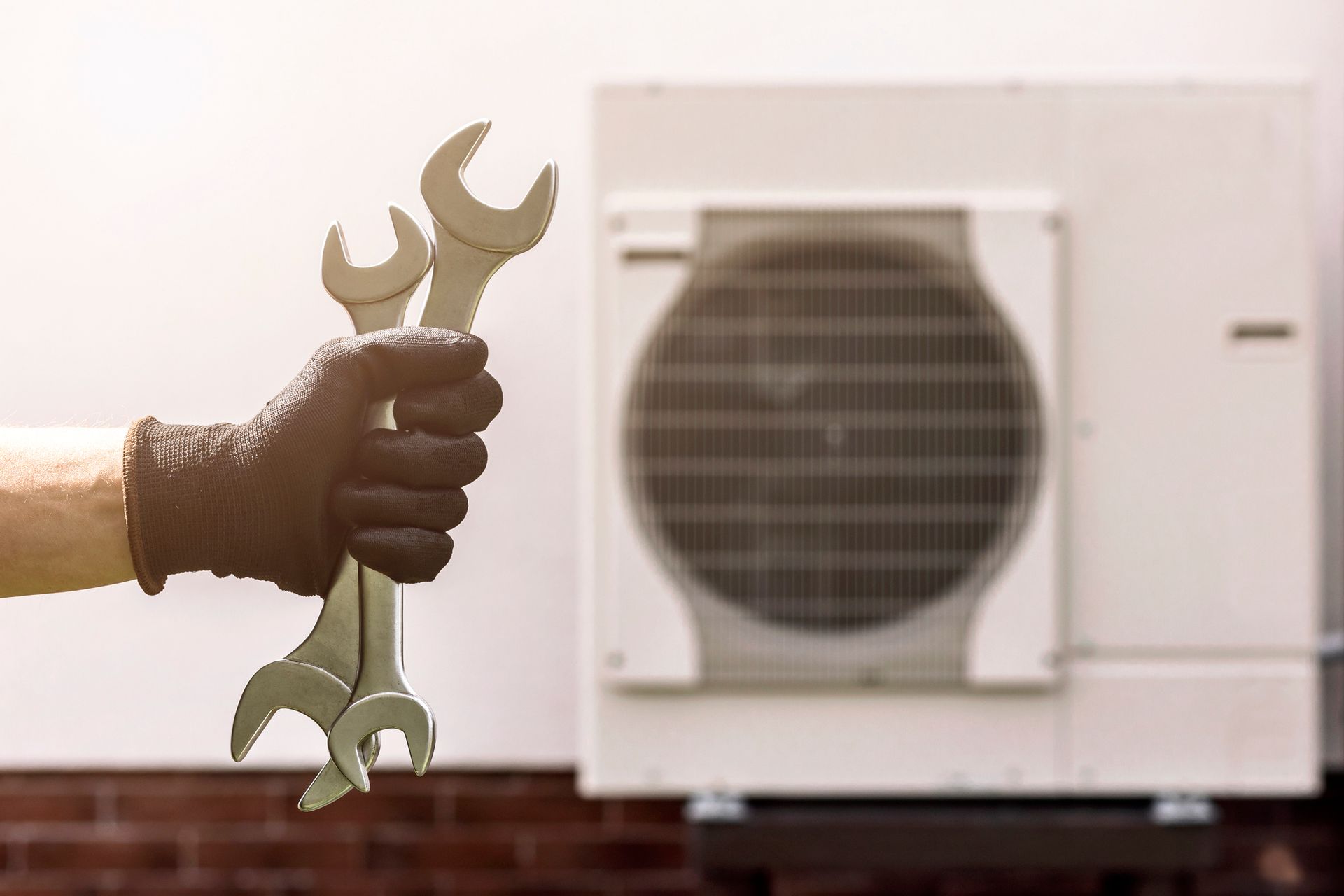 Person in black gloves holding wrenches in front of an outdoor air conditioning unit.