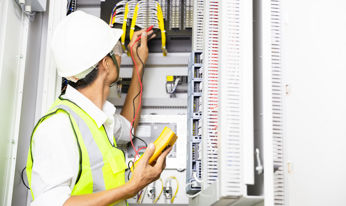 An electrician is working on an electrical box while holding a multimeter. An electrician is working on an electrical box while holding a multimeter.