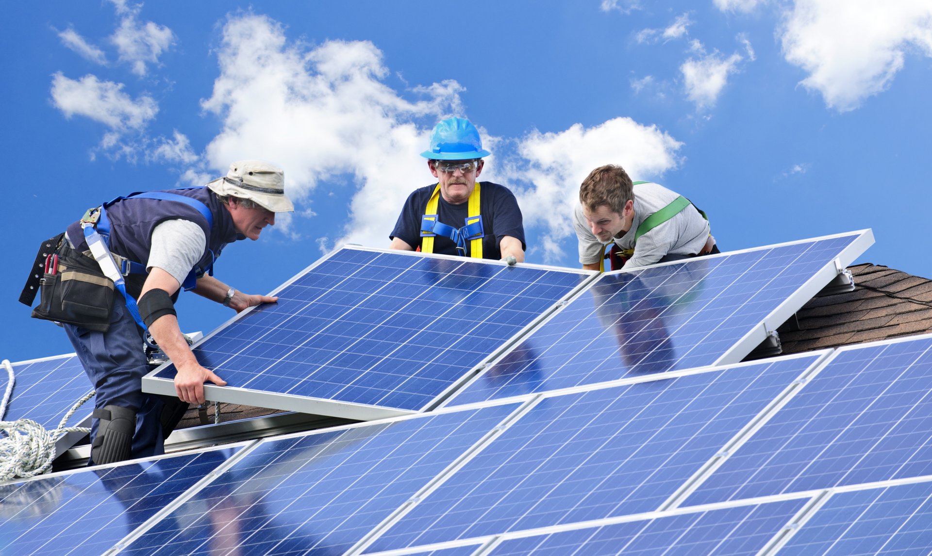 Workers install solar panels on a rooftop against a blue sky.