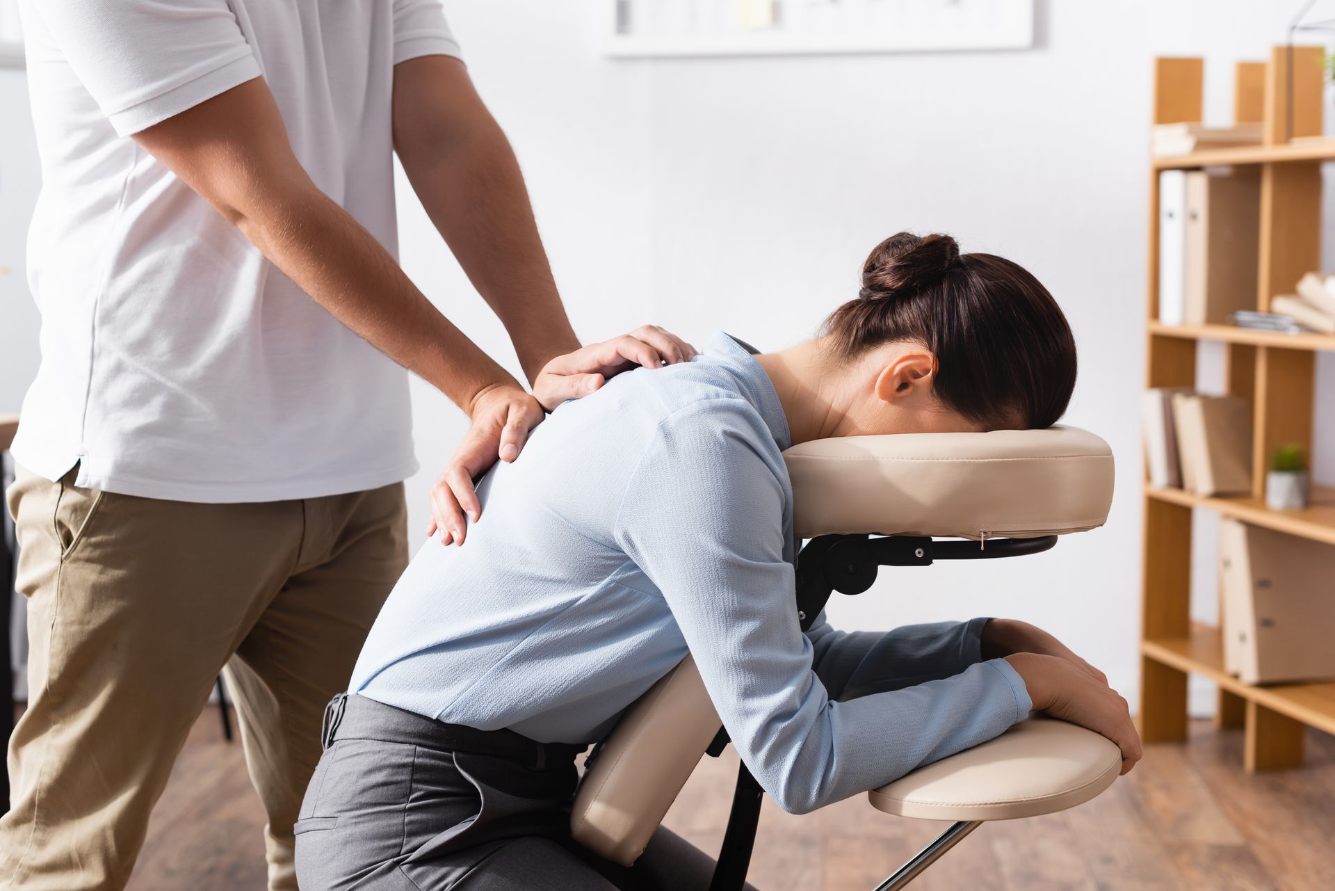 Person receiving a seated massage while another person applies pressure to the back.